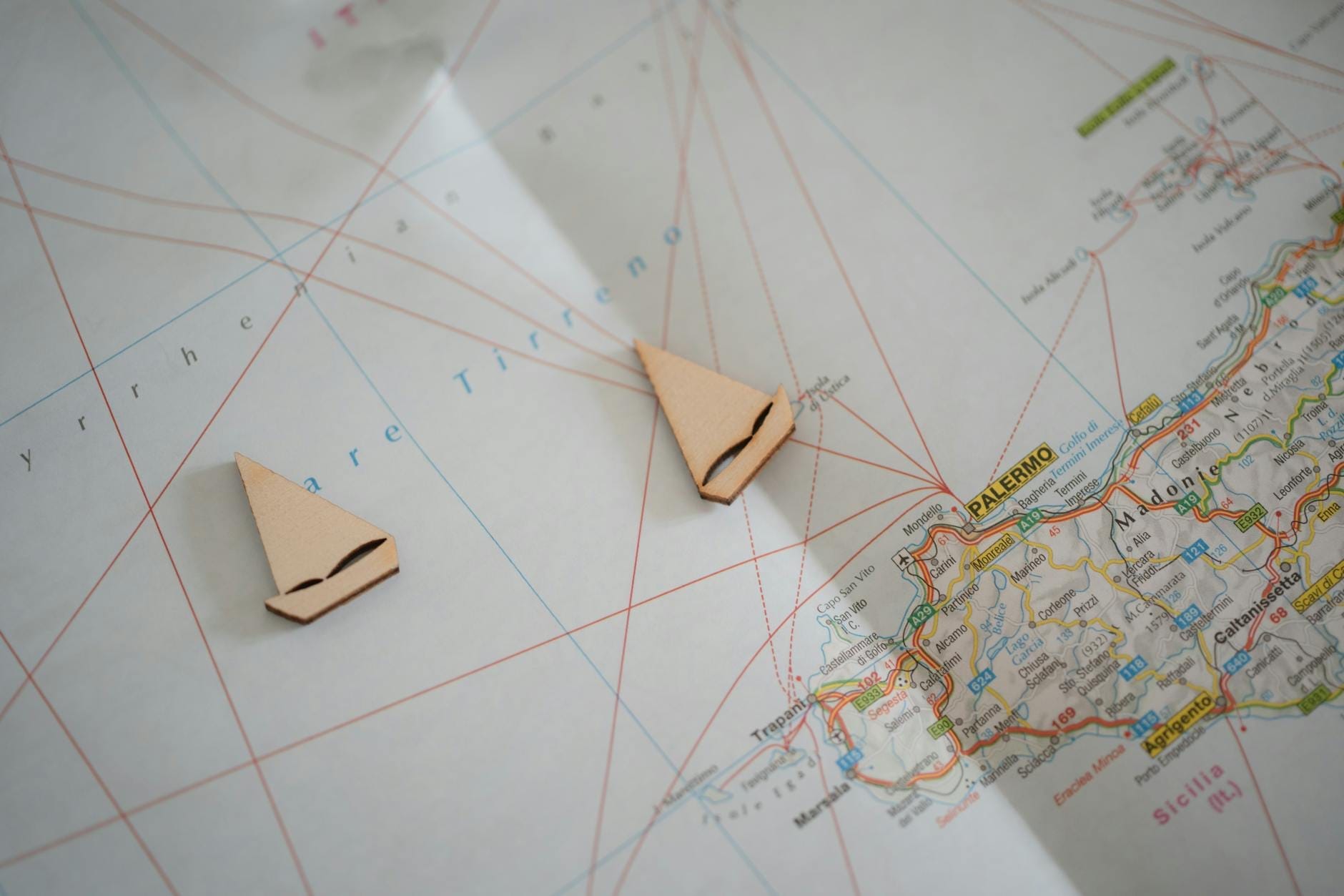 Nahaufnahme einer Sizilien-Karte mit Palermo und Küstenrouten, auf der zwei kleine hölzerne Segelboot-Marker platziert sind.