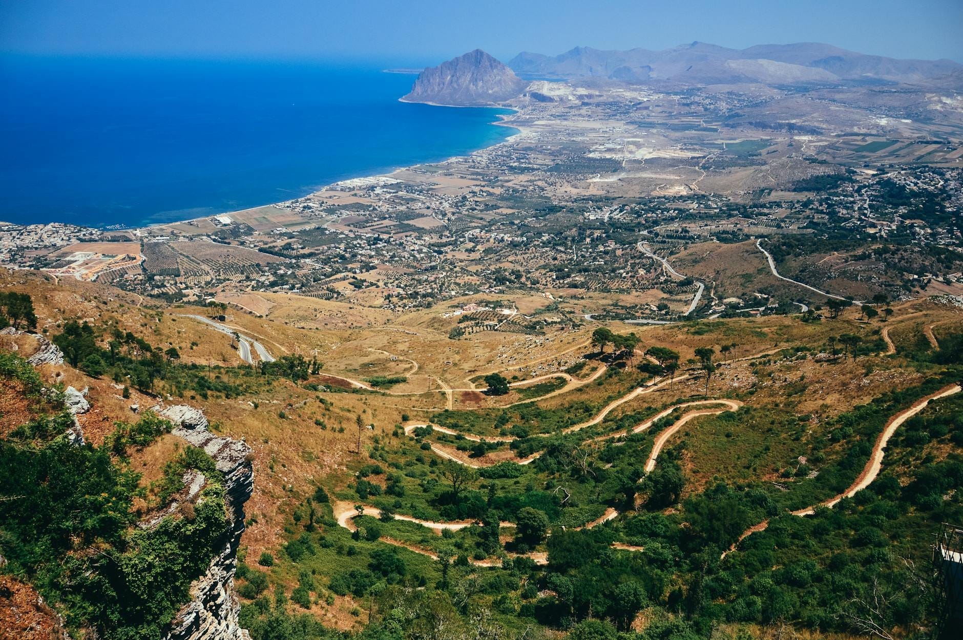 Kurvenreiche Bergstraßen, die zu einer malerischen sizilianischen Küste mit blauem Wasser und schroffen Hügeln hinabführen – ideal für ein Roadtrip-Abenteuer.