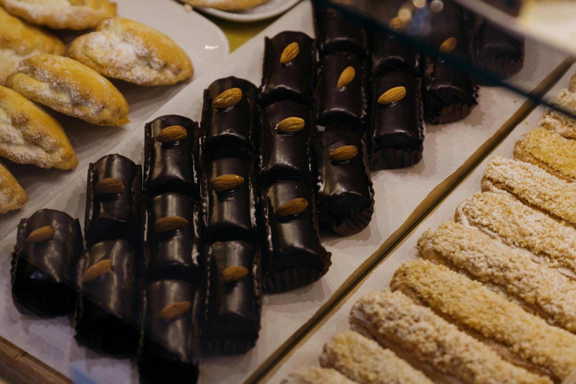 Tablett mit verschiedenen sizilianischen Gebäckstücken, darunter schokoladenüberzogene Mandelsüßigkeiten und andere traditionelle italienische Desserts in einer Bäckereivitrine.