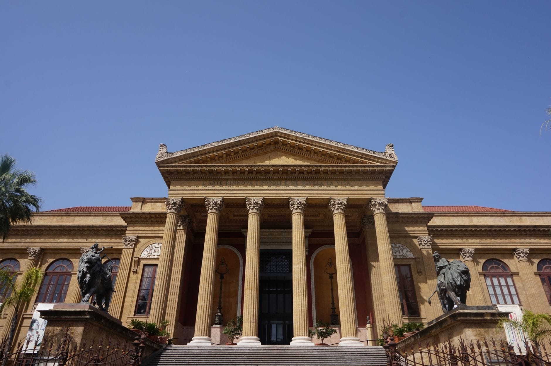 Vorderansicht des Teatro Massimo in Palermo mit imposanten Säulen und Statuen unter einem klaren blauen Himmel.