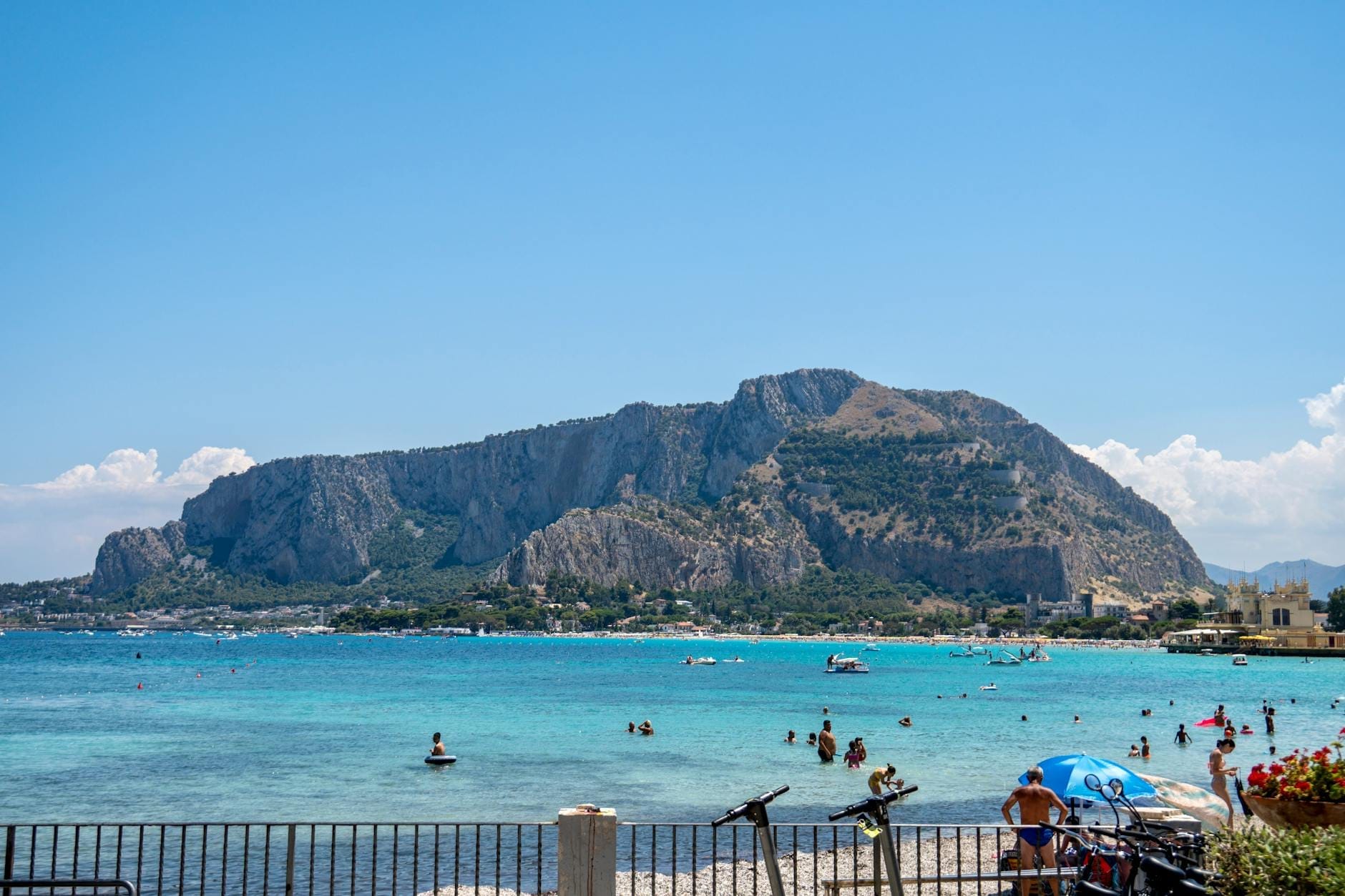 Klare Aussicht auf den Mondello Beach auf Sizilien mit Schwimmern im Meer, leuchtend türkisblauem Wasser, Bergen im Hintergrund und einem sonnigen Tag.
