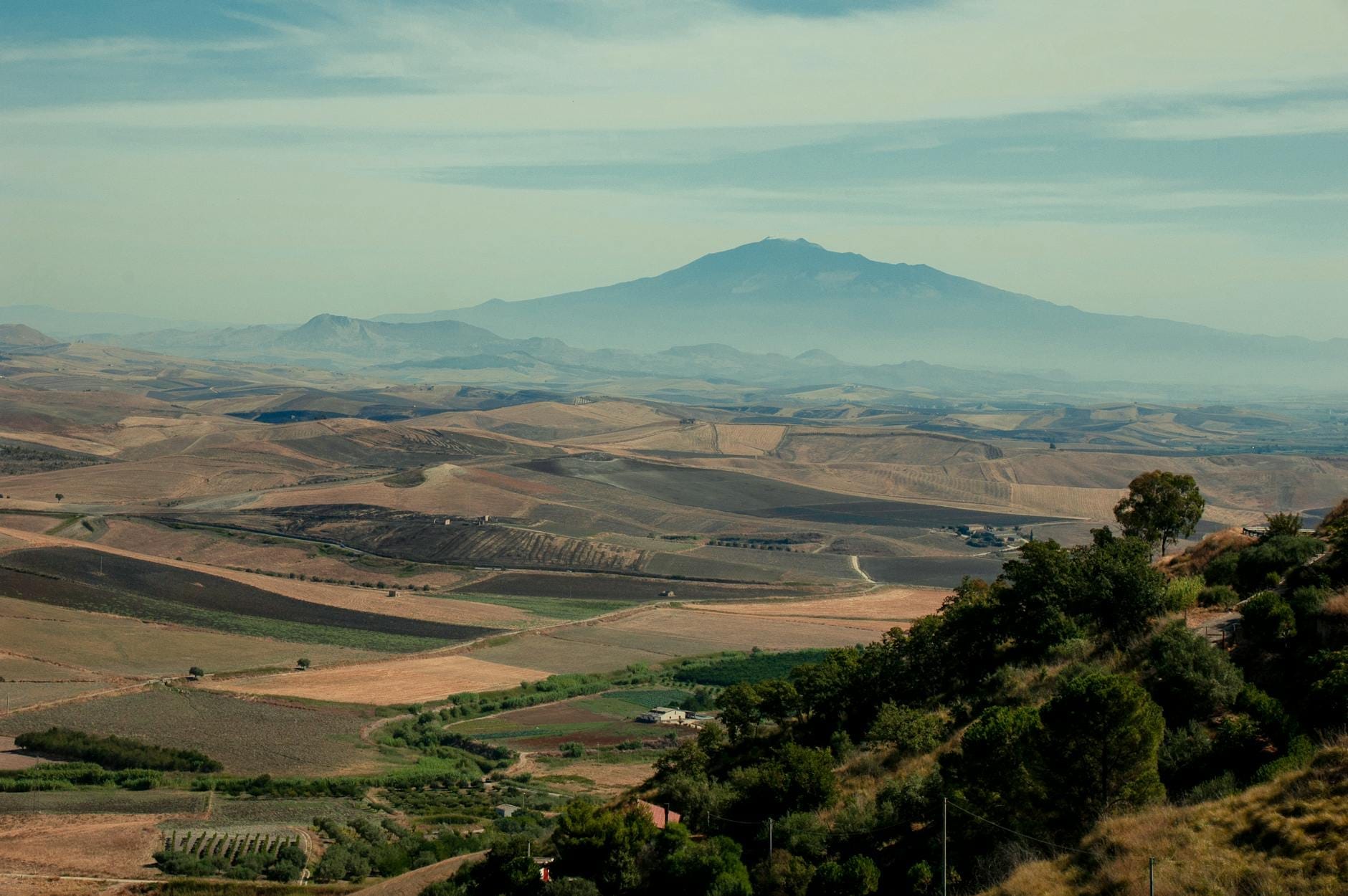 Blick über sanfte Hügel und Ackerland mit einem fernen Berg in Sizilien, unter einem dunstigen Oktoberhimmel.