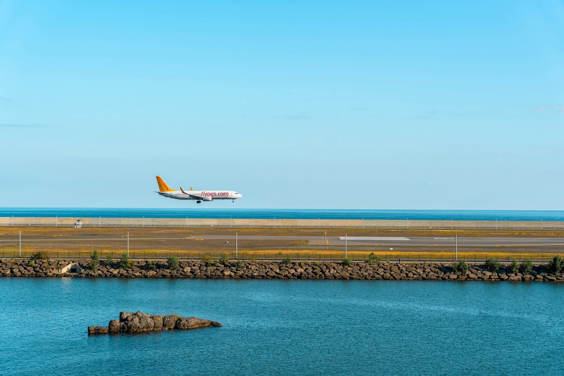 Ein Flugzeug landet auf einer Landebahn am Meer, mit blauem Himmel und Wasser, und zeigt eine typische Ankunftsszene am Flughafen auf Sizilien.