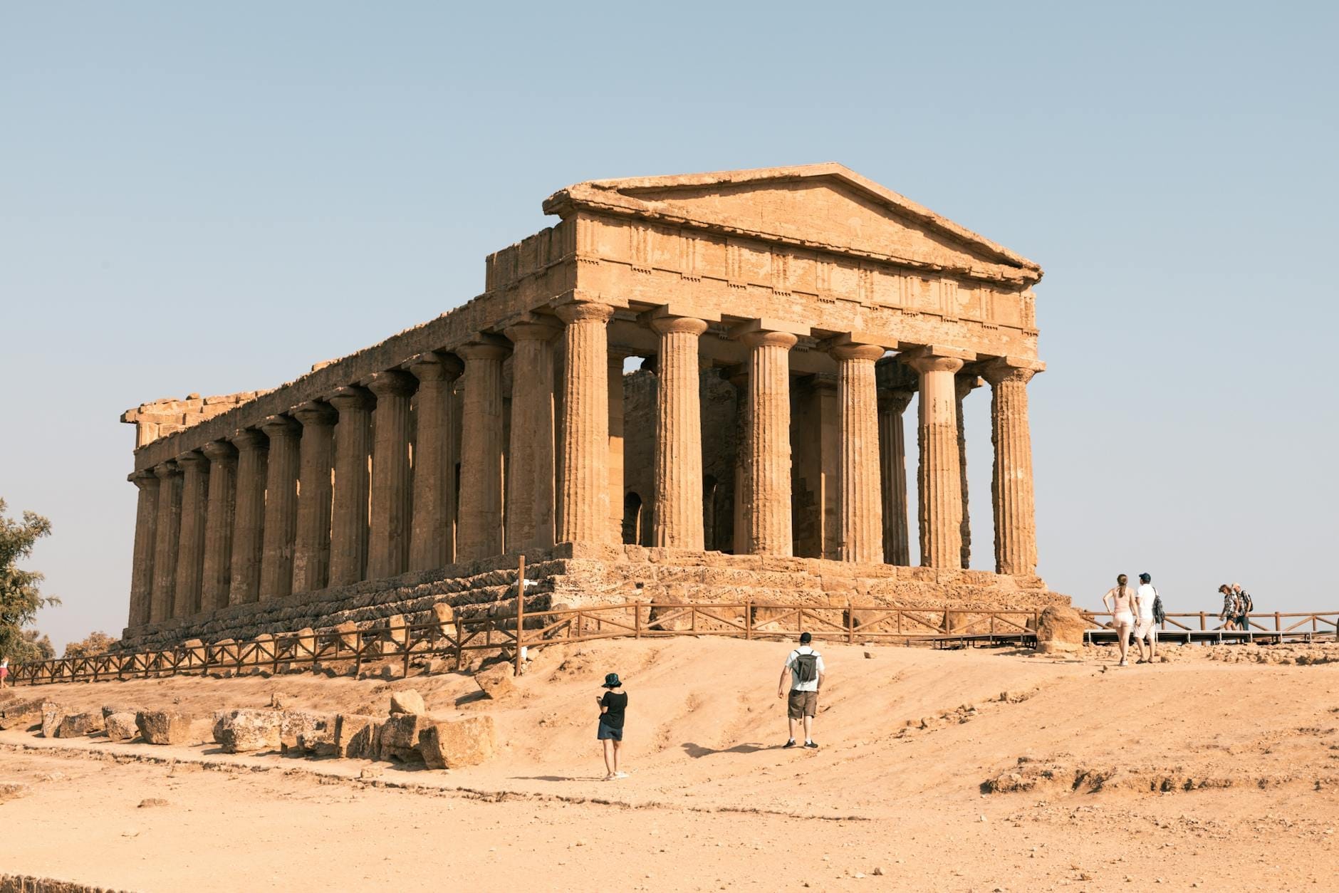 Besucher schlendern um den sonnenbeschienenen Tempel der Concordia in Agrigento, Sizilien, an einem heißen, trockenen Sommertag mit klarem Himmel.