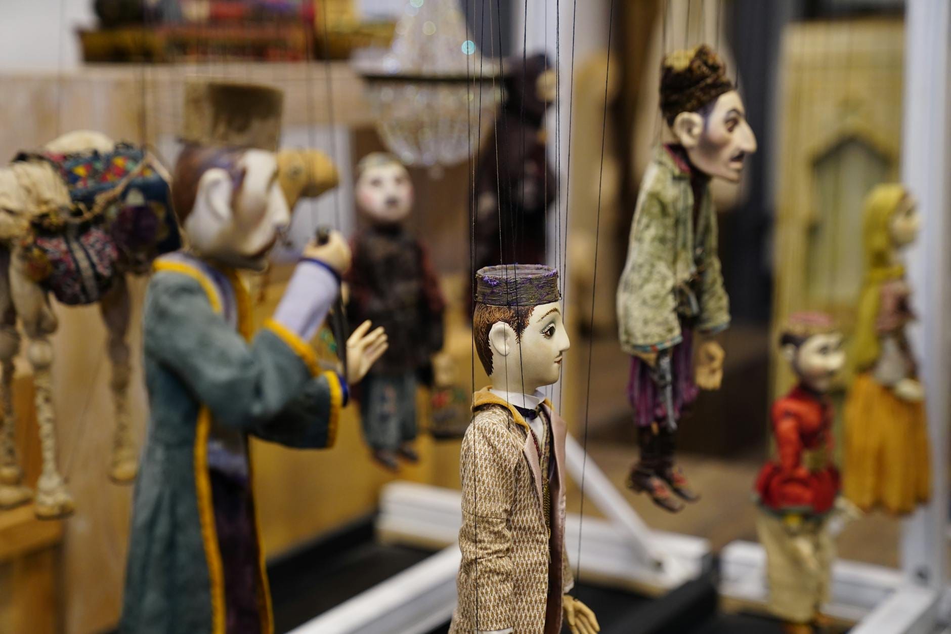 Mehrere aufwendig gestaltete Puppen, die an Fäden in einem kleinen, intimen Theaterraum hängen, und die Atmosphäre sizilianischer Puppenspiele heraufbeschwören.