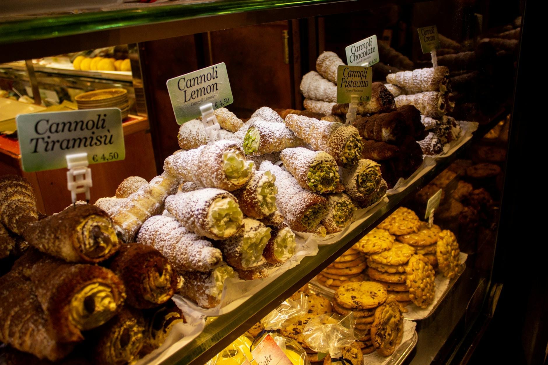 Glasvitrine gefüllt mit verschiedenen Cannoli-Sorten, bestäubt mit Puderzucker, in einer sizilianischen Konditorei.