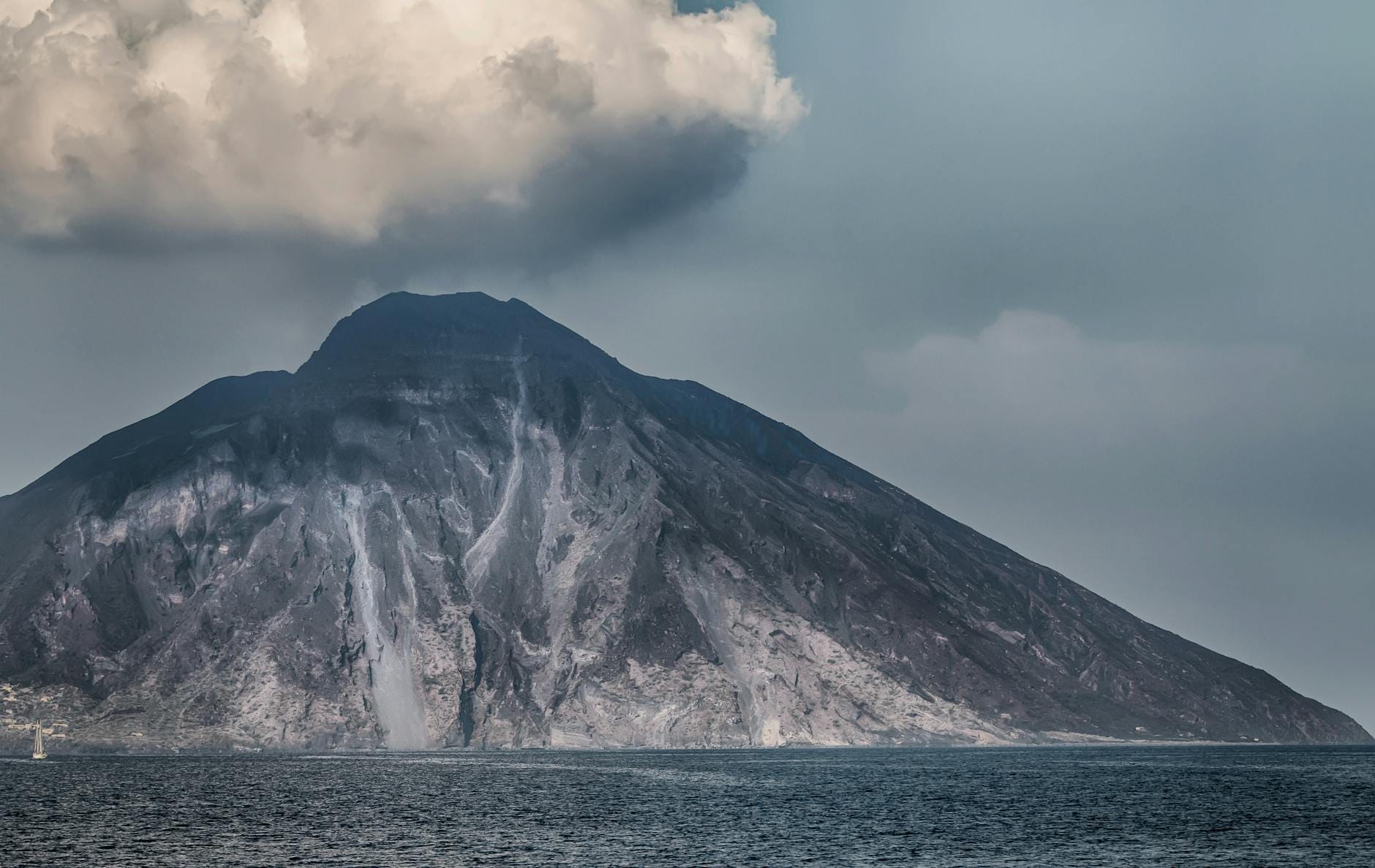 Ein beeindruckender Blick auf den Vulkan Stromboli, der aus dem Meer aufragt, mit Rauch am Gipfel unter einem bewölkten Himmel.