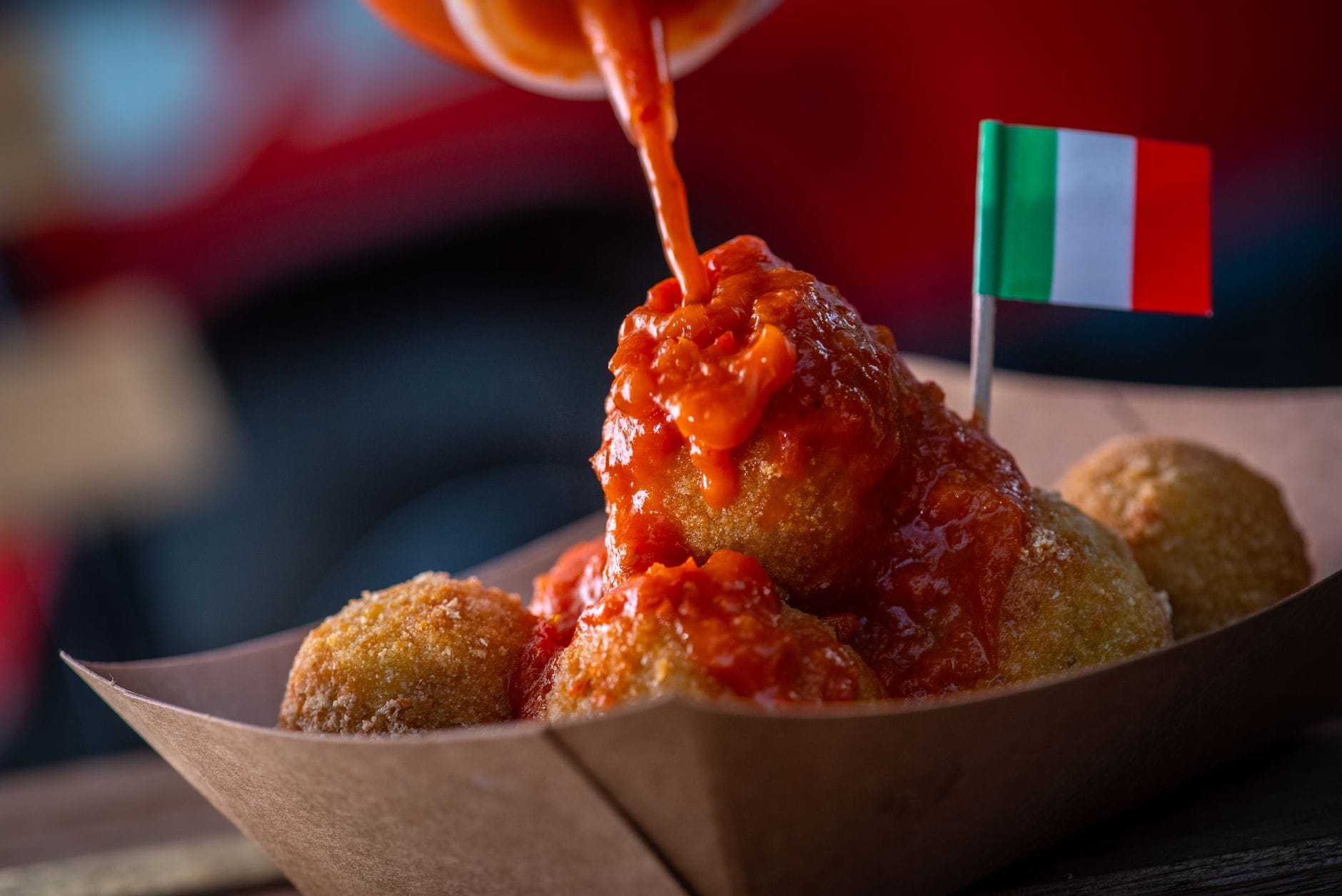 Nahaufnahme von Arancini mit darüber gegossener Tomatensauce, serviert in einem Papptablett mit einer kleinen italienischen Flagge.