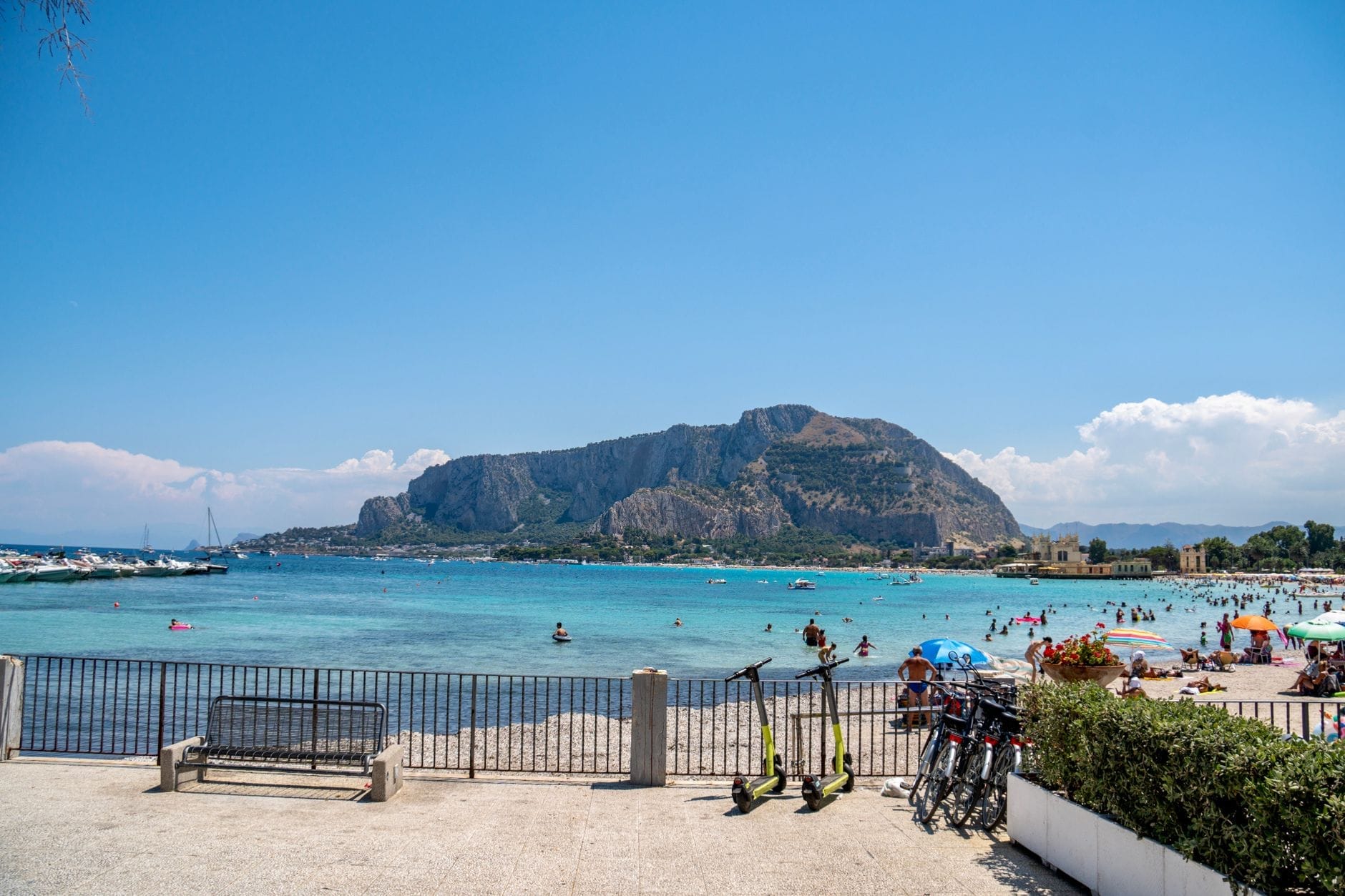 Sandstrand mit Menschen, die in flachem türkisfarbenem Wasser schwimmen und spielen, mit einem Berg und klarem blauem Himmel im Hintergrund in Sizilien.