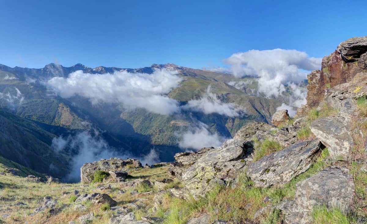 ยอดเขาและสันเขาหินสูงของ Sierra Nevada ใต้ท้องฟ้าสีฟ้ากับกลุ่มเมฆ เห็นระดับความสูงและหุบเขาเขียวด้านล่าง