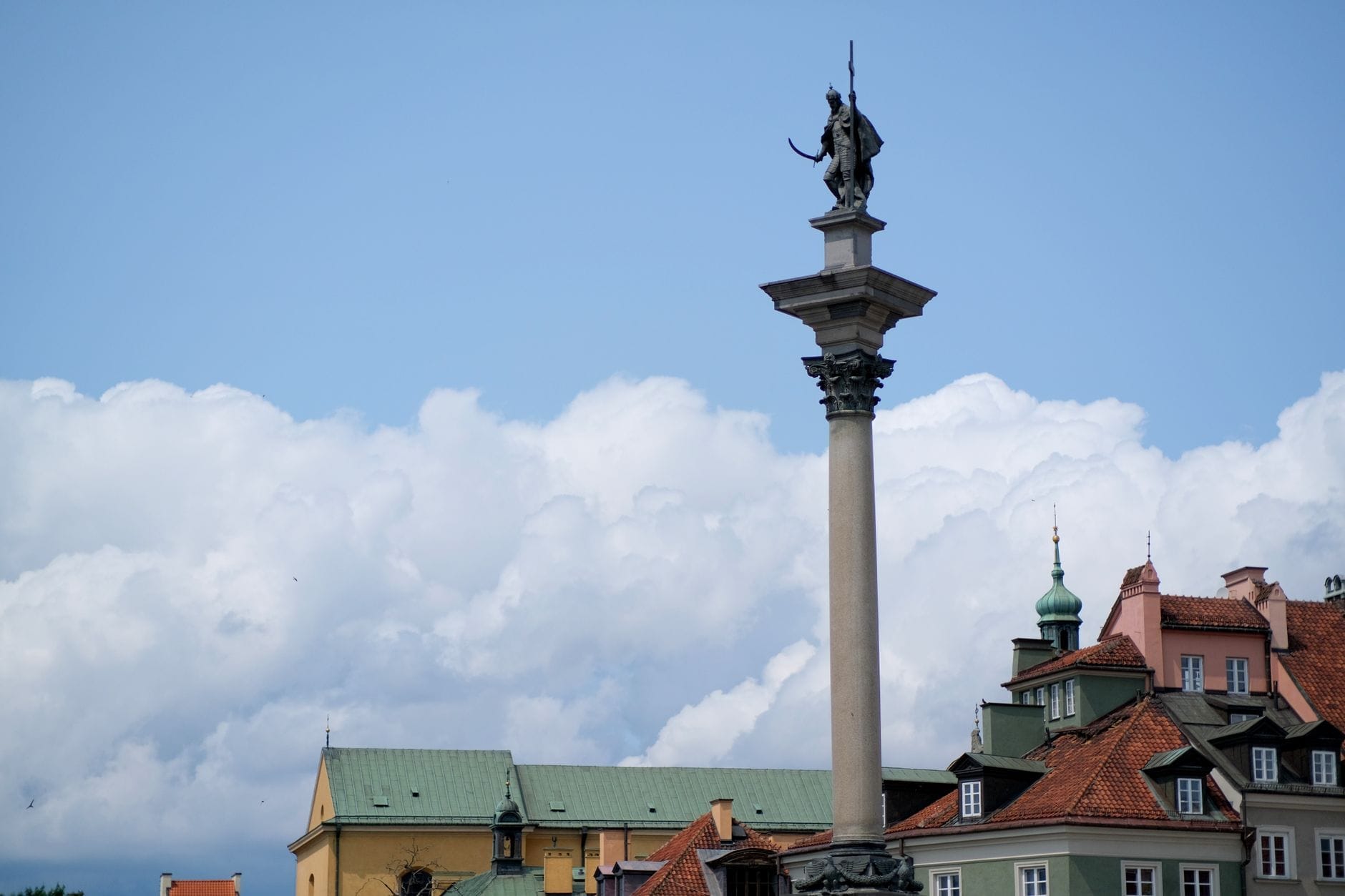 เสา Sigismund ตั้งตระหง่านเหนืออาคารสีสันสดใสบริเวณ Castle Square ในกรุงวอร์ซอ ท่ามกลางท้องฟ้าสีฟ้าสดใสและเมฆขาว