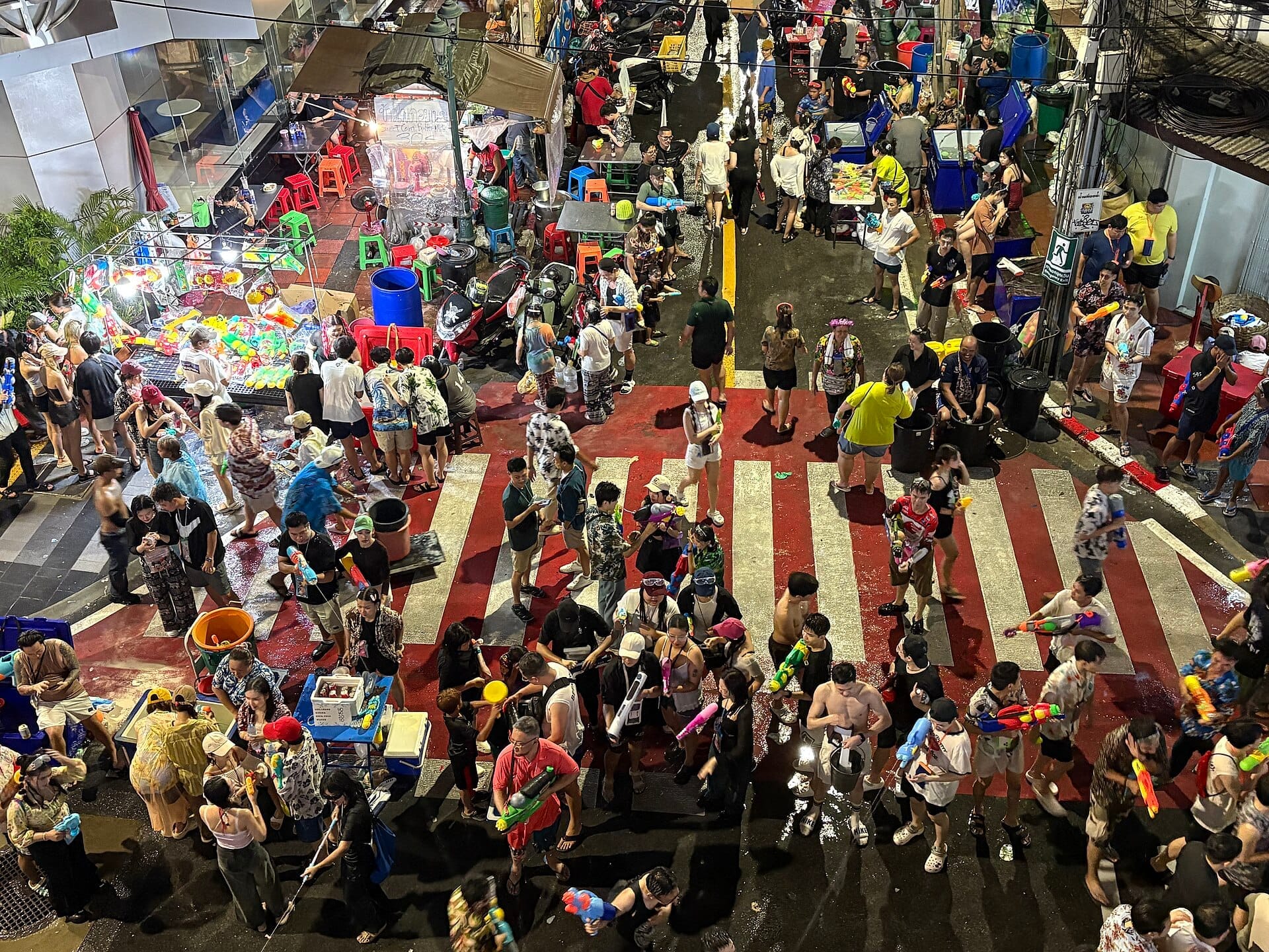 Folla che festeggia il Songkran su Silom Road a Bangkok con battaglie d'acqua, bancarelle e atmosfera notturna