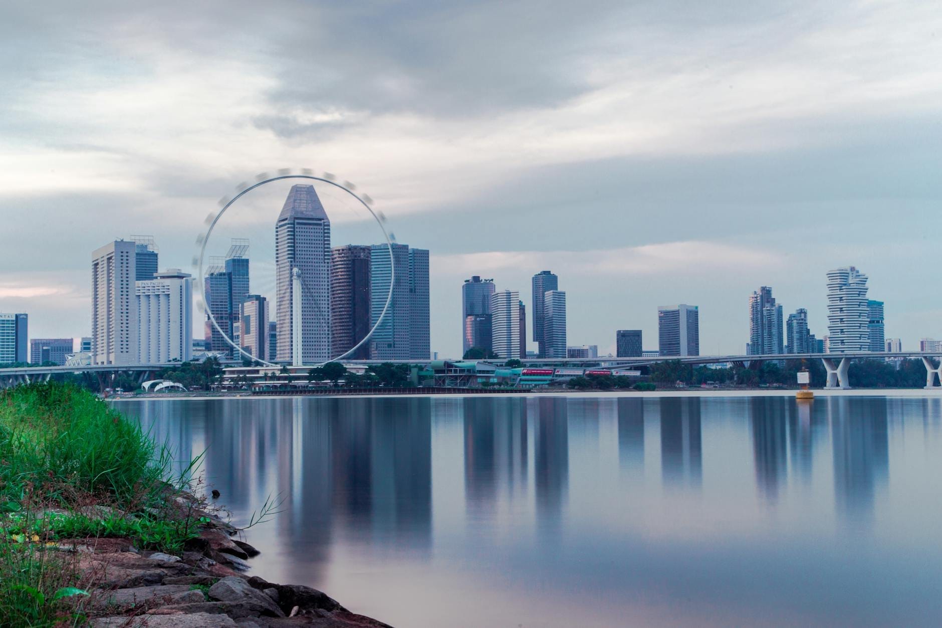 วิวชิงช้าสวรรค์ Singapore Flyer ตระหง่านเหนือสกายไลน์ Marina Bay สะท้อนเงาลงบนผืนน้ำยามพลบค่ำอย่างงดงาม
