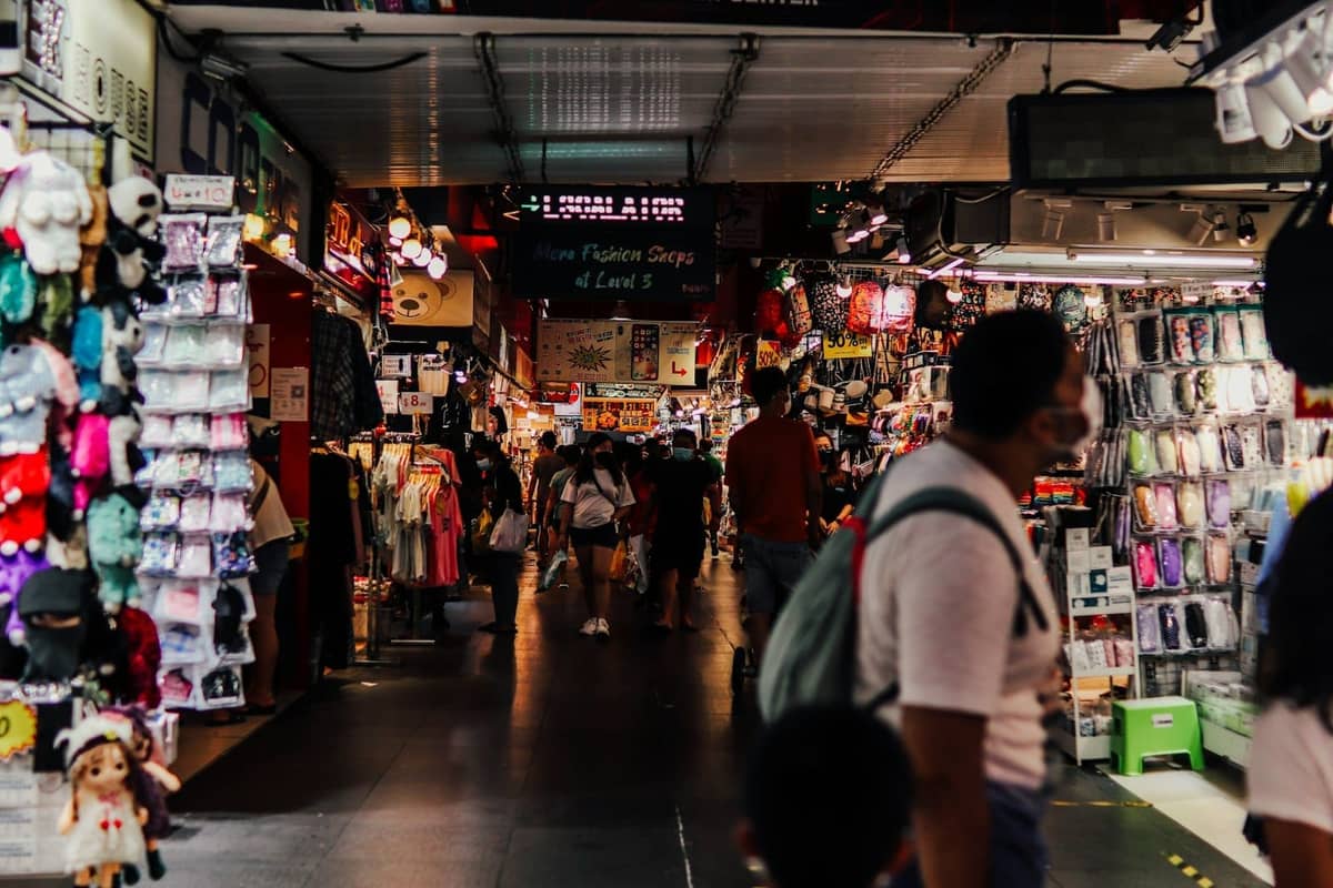 Indoor market scene with busy walkways, budget clothing, accessories, souvenirs, and shoppers at stalls, typical of Singapore's bargain shopping spots.