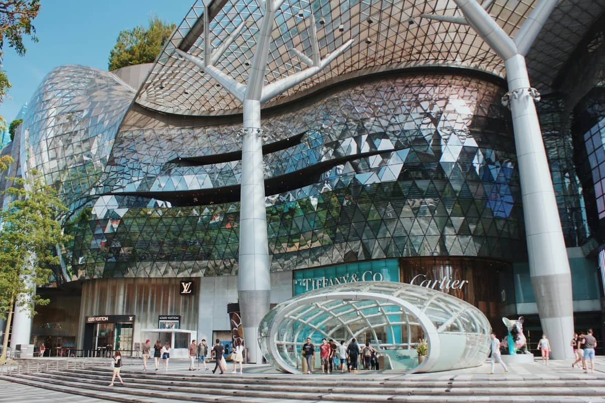 Modern glass facade of a major Orchard Road shopping mall with luxury brand storefronts and people walking outside in Singapore.