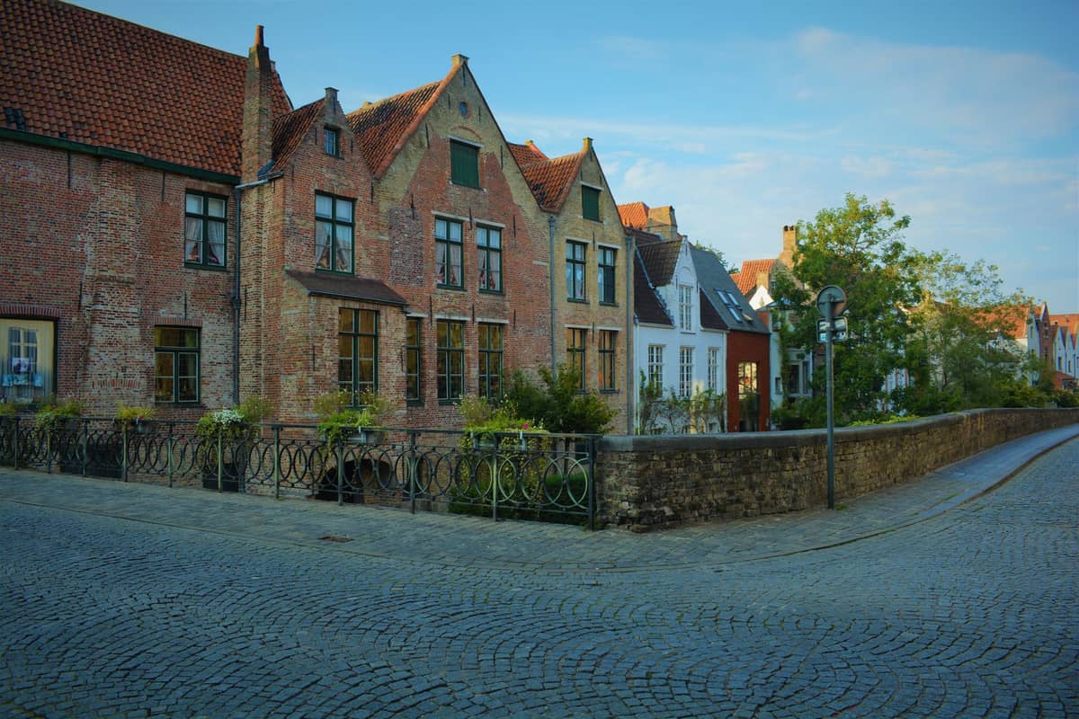 A quiet cobblestone street lined with gabled brick houses and trees in the Sint-Anna Quarter of Bruges, capturing the local residential charm.