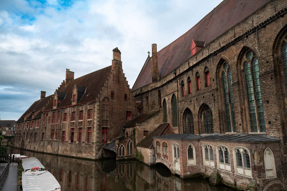 Oblique view of the brick and gothic arched windows of Museum Sint-Janshospitaal in Bruges beside the canal, showing the medieval exterior under a blue sky.