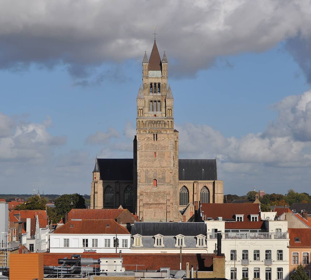 Sint-Salvatorskathedraal rises above Bruges’ red-roofed buildings under a partly cloudy sky, showcasing its Romanesque and Gothic architecture.