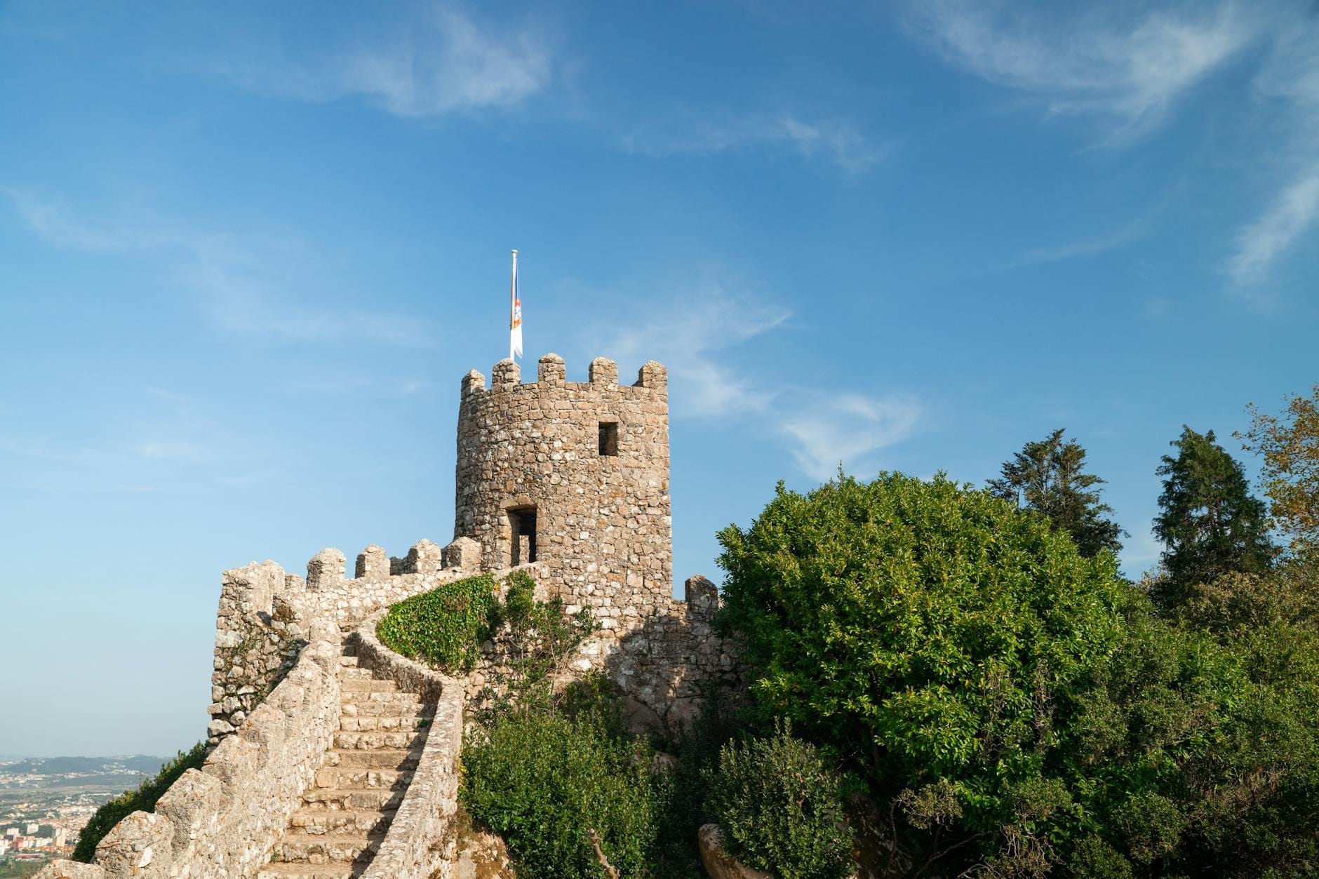 Marches en pierre serpentant jusqu'aux créneaux du Castelo dos Mouros à Sintra avec ciel bleu et verdure.