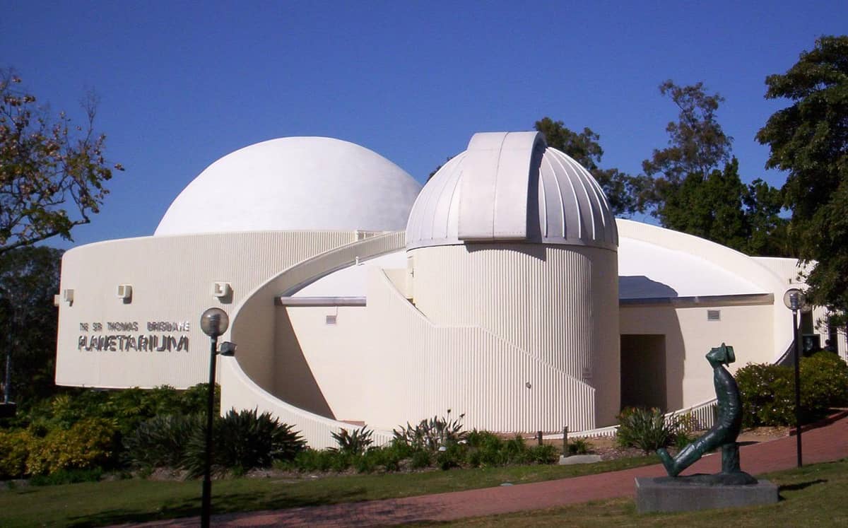 The exterior of the Sir Thomas Brisbane Planetarium in Brisbane, showing its distinctive white domes and observatory against a clear blue sky.
