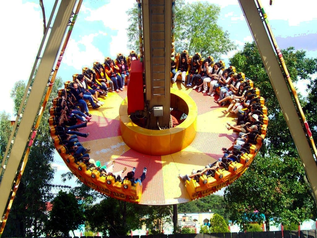 Grande giostra circolare piena di persone a Six Flags México, circondata da alberi verdi e un cielo luminoso e soleggiato.