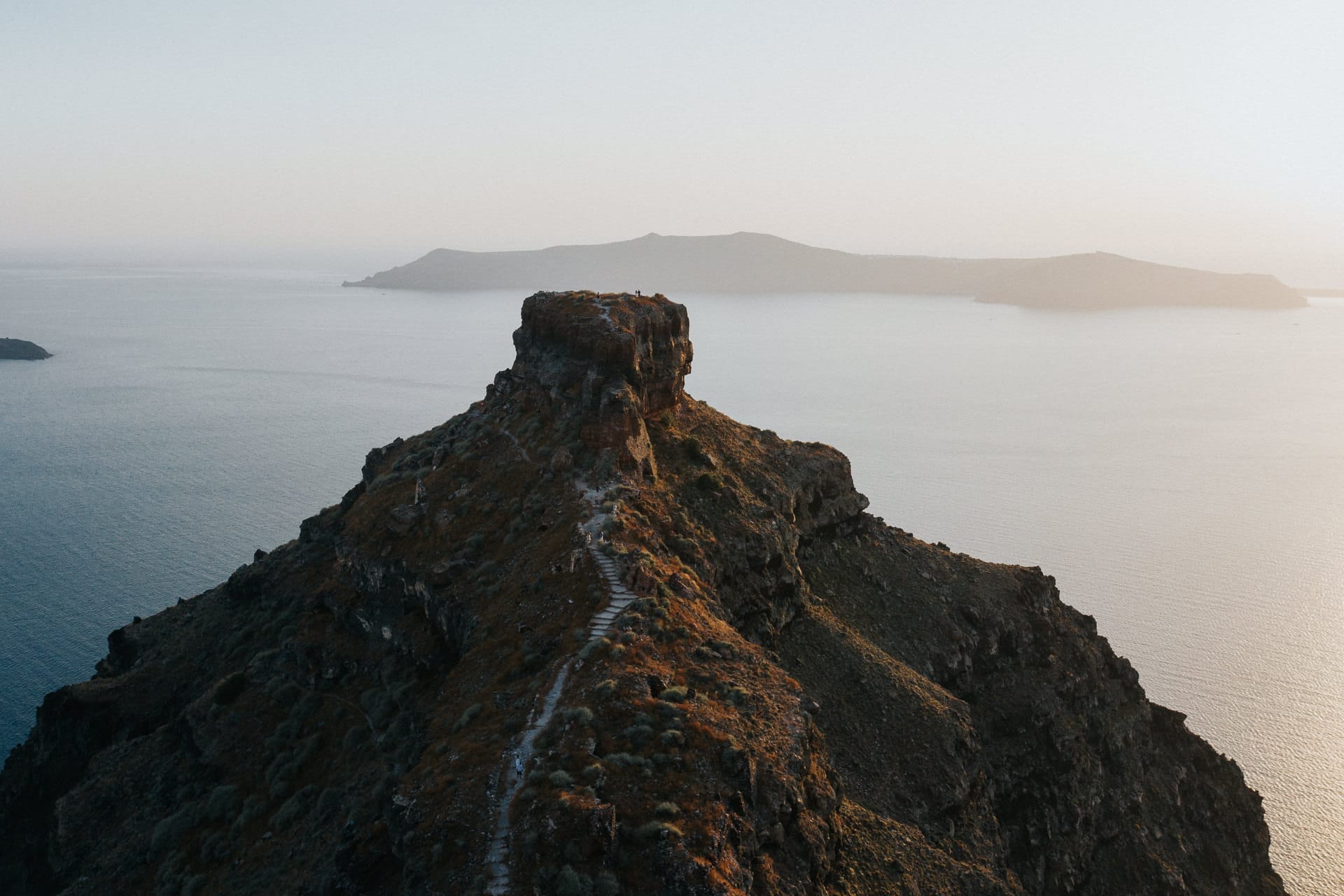 เส้นทางขรุขระนำขึ้นสู่ Skaros Rock ใน Imerovigli ที่ตั้งอยู่บนหน้าผาเหนือน้ำสีฟ้าของปล่องภูเขาไฟ Santorini ในยามพระอาทิตย์ตก