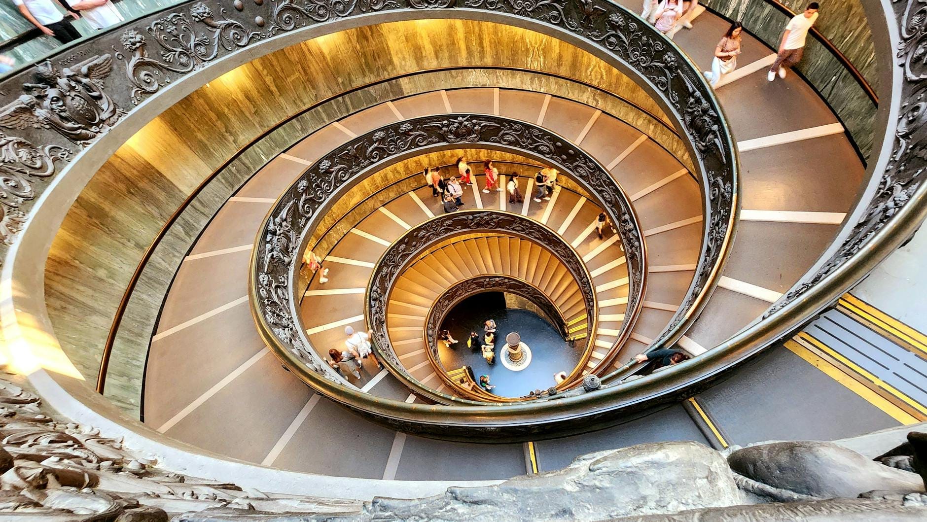 Looking down the iconic spiral staircase at the Vatican Museums with people ascending and descending the steps.