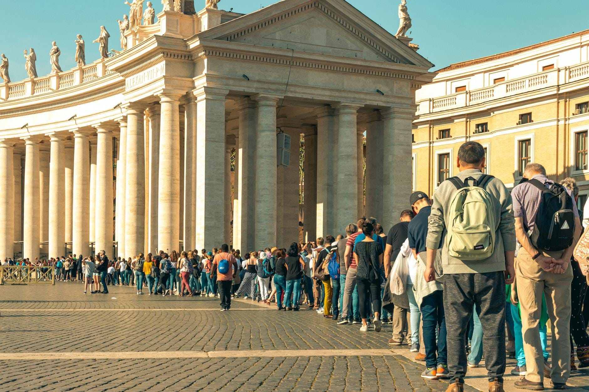 Long line of tourists waiting outside a grand Roman columned building under a bright sky, illustrating queue times at major attractions in Rome.