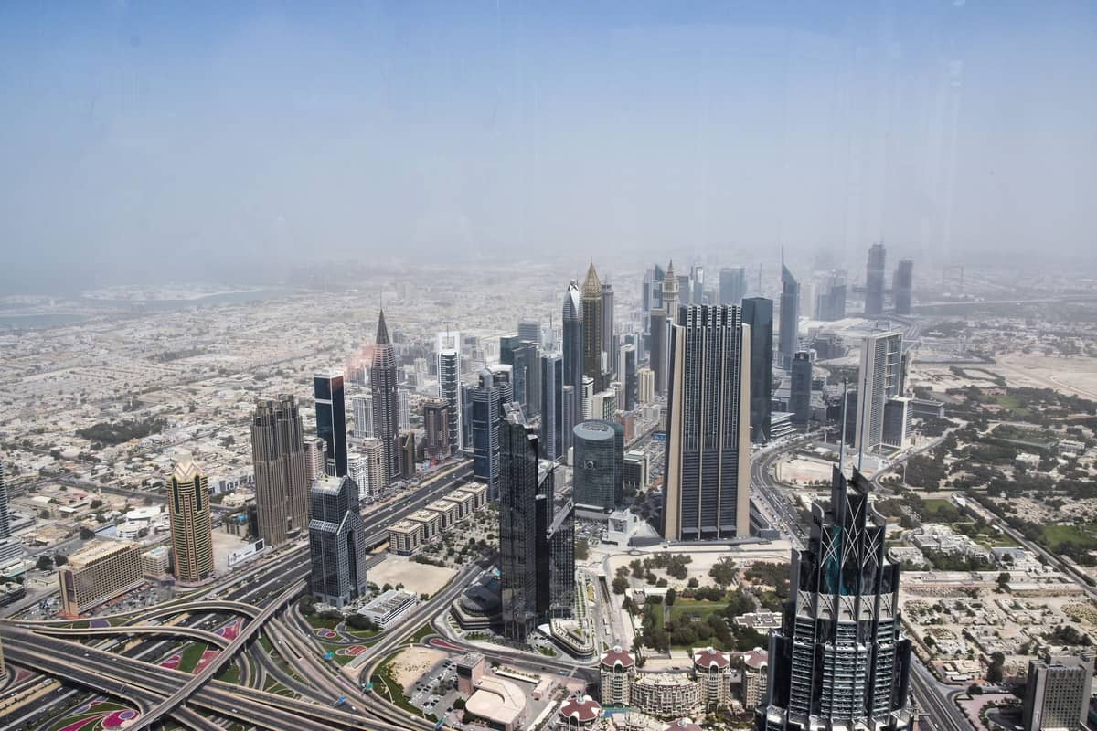 Blick von einem hohen Aussichtspunkt in Dubai auf die Downtown-Skyline mit modernen Wolkenkratzern, dem Sheikh Zayed Road und der Wüstenlandschaft unter einem strahlend blauen Mittagshimmel.