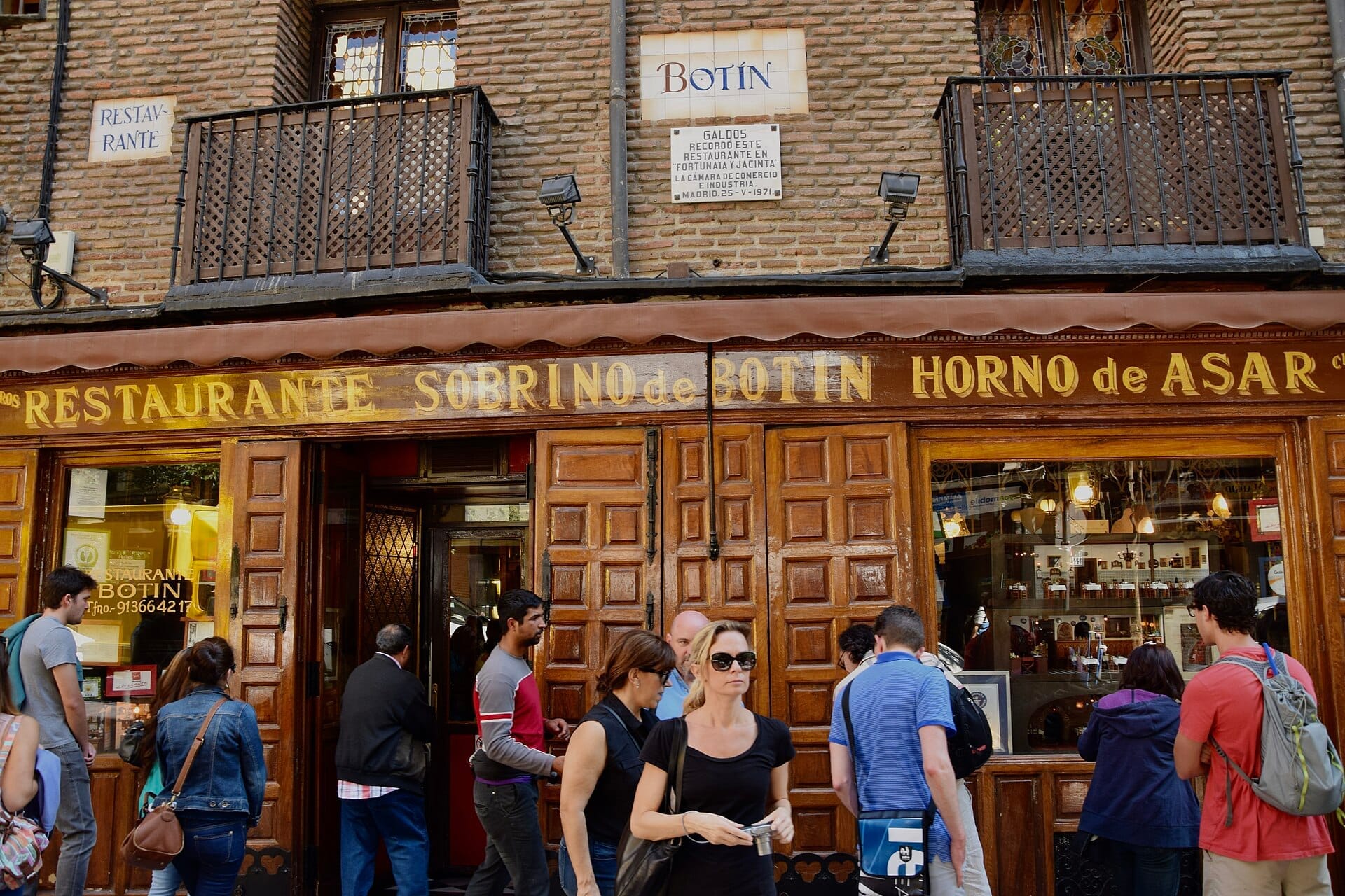 Ingresso del ristorante Sobrino de Botín con classiche porte in legno, facciata in mattoni e persone riunite fuori di giorno.