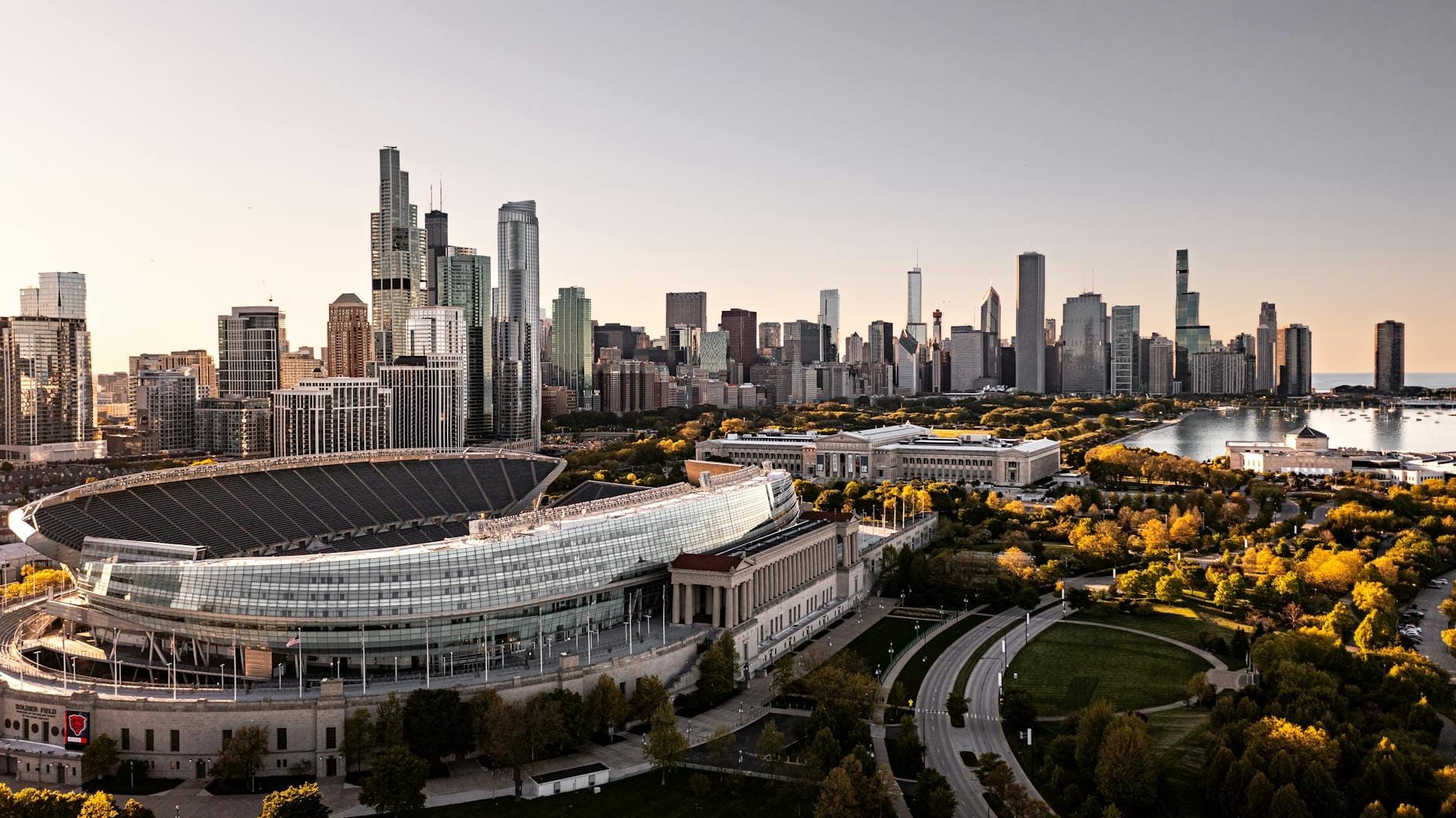Vista aerea di Soldier Field con lo skyline di Chicago e il lago Michigan sullo sfondo in una giornata limpida, che mostra l'architettura dello stadio e il parco circostante.