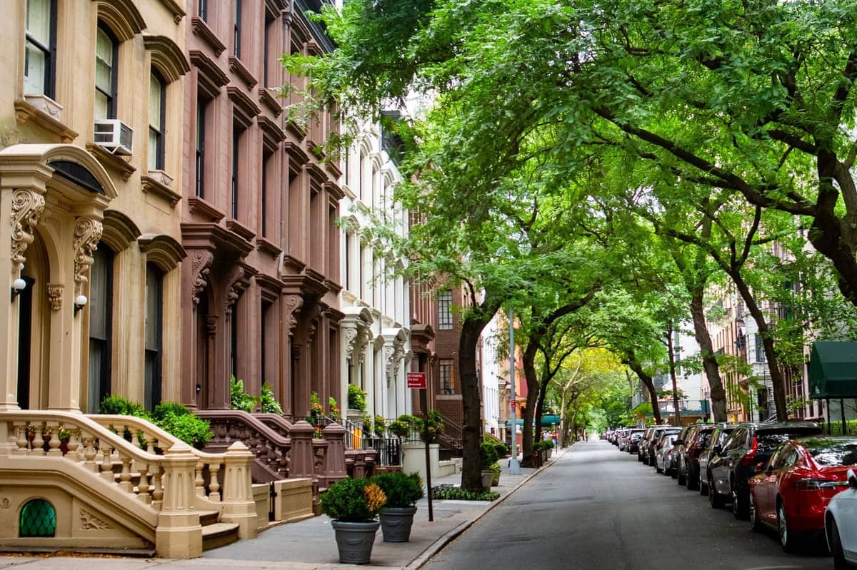 Baumgesäumte Straße in New York City mit klassischen Brownstone-Reihenhäusern und geparkten Autos, die eine wohnliche Nachbarschaftsatmosphäre einfängt.