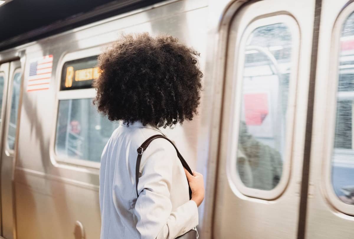 Eine Frau wartet auf einem U-Bahnsteig, während ein NYC-U-Bahn-Zug der Linie R in die Station einfährt.