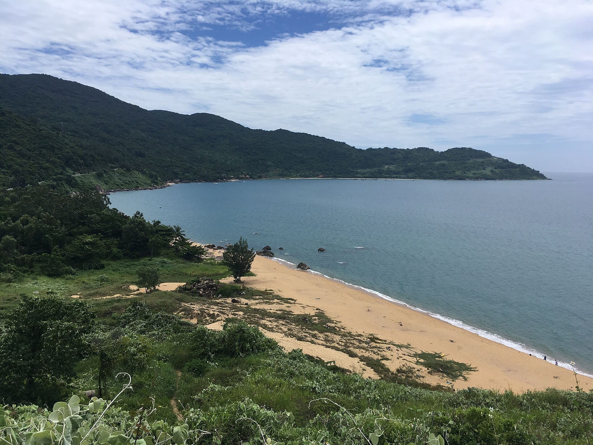 วิวหาดทรายสงบบนคาบสมุทรเซินจ่า มีป่าทึบด้านหลัง คลื่นแผ่ว ๆ กับต้นไม้เขียวในเฟรม