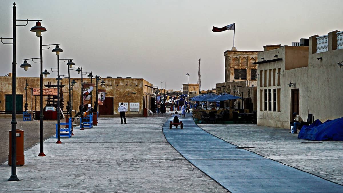 Traditionelle Korallensteingebäude, Marktbuden und Laternenmasten säumen die breiten Wege des Souq Al Wakra unter einem dunstigen Himmel in Katar.