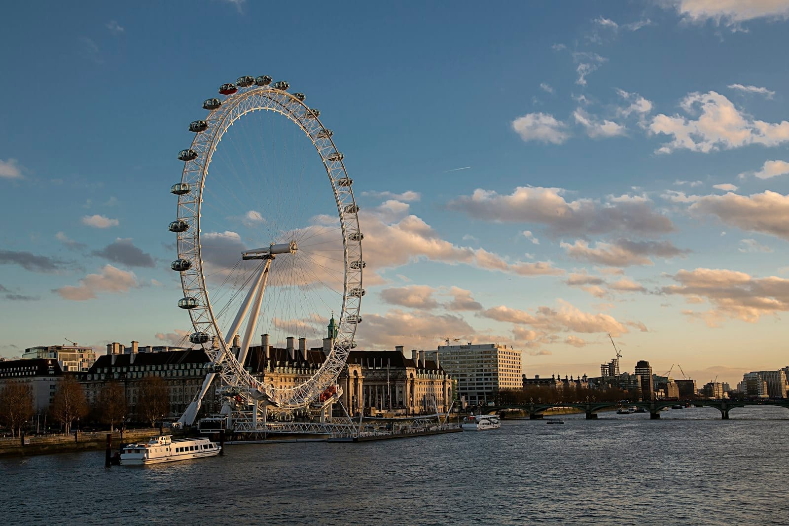 ลอนดอนอายและอาคารริม South Bank ที่อาบแสงเย็นริมแม่น้ำเทมส์ เบื้องหน้าเป็นน้ำและท้องฟ้าฟ้าใสมีเมฆบาง ๆ