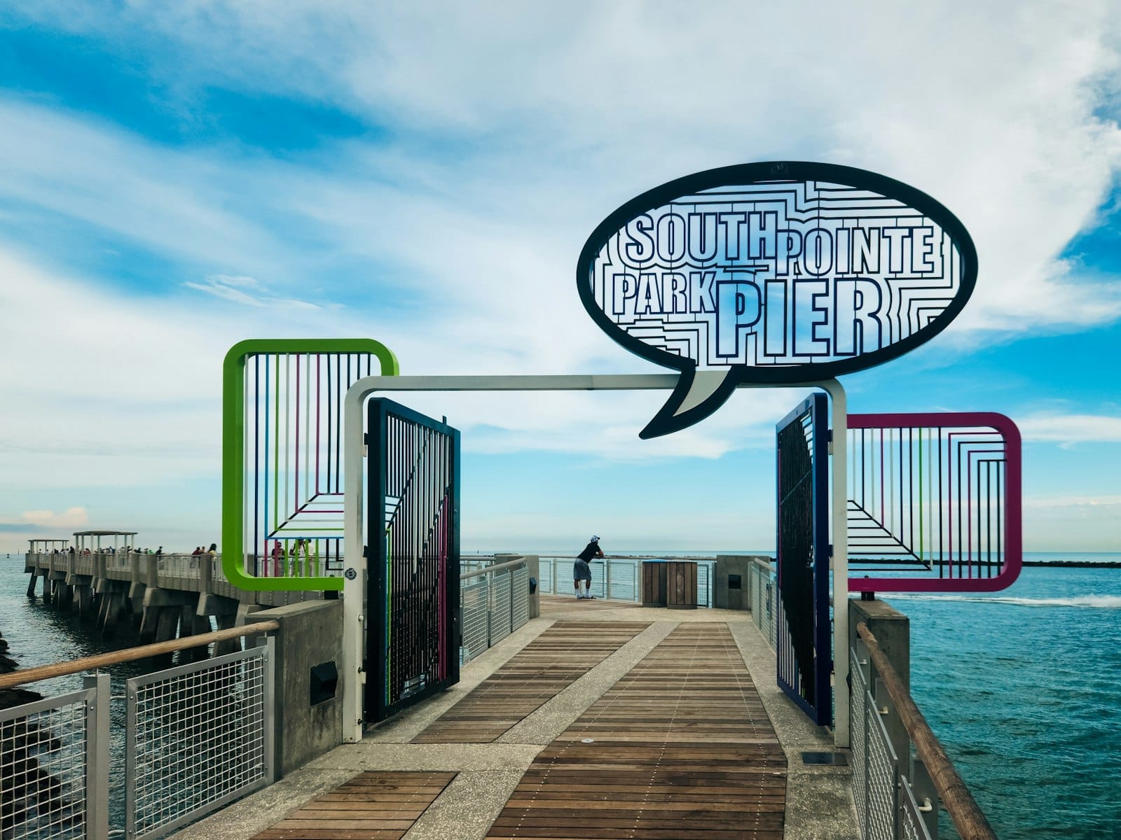 Ingresso al South Pointe Park Pier a Miami Beach, con arte colorata, un grande cartello, cielo azzurro limpido e acque oceaniche calme.