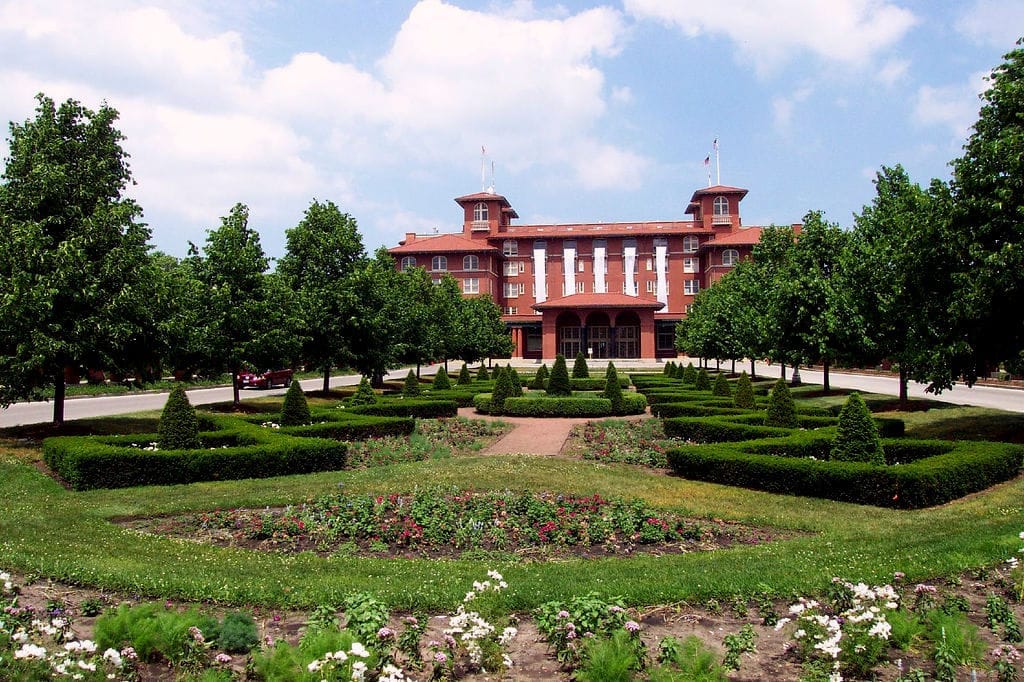 South Shore Cultural Center in mattoni rossi con giardino simmetrico, siepi curate e lussureggianti alberi verdi sotto un cielo azzurro brillante.