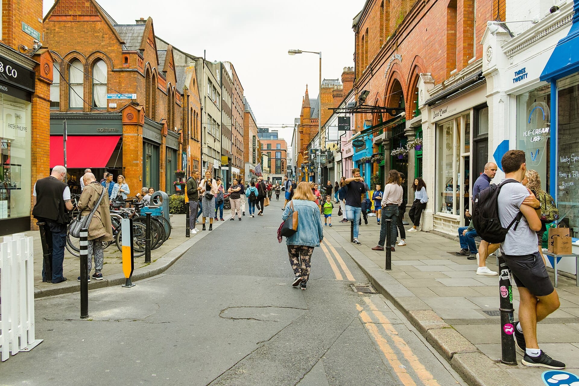 I pedoni passeggiano lungo South William Street a Dublino, fiancheggiata da edifici georgiani in mattoni rossi, negozi indipendenti e vivaci vetrine in una giornata nuvolosa.