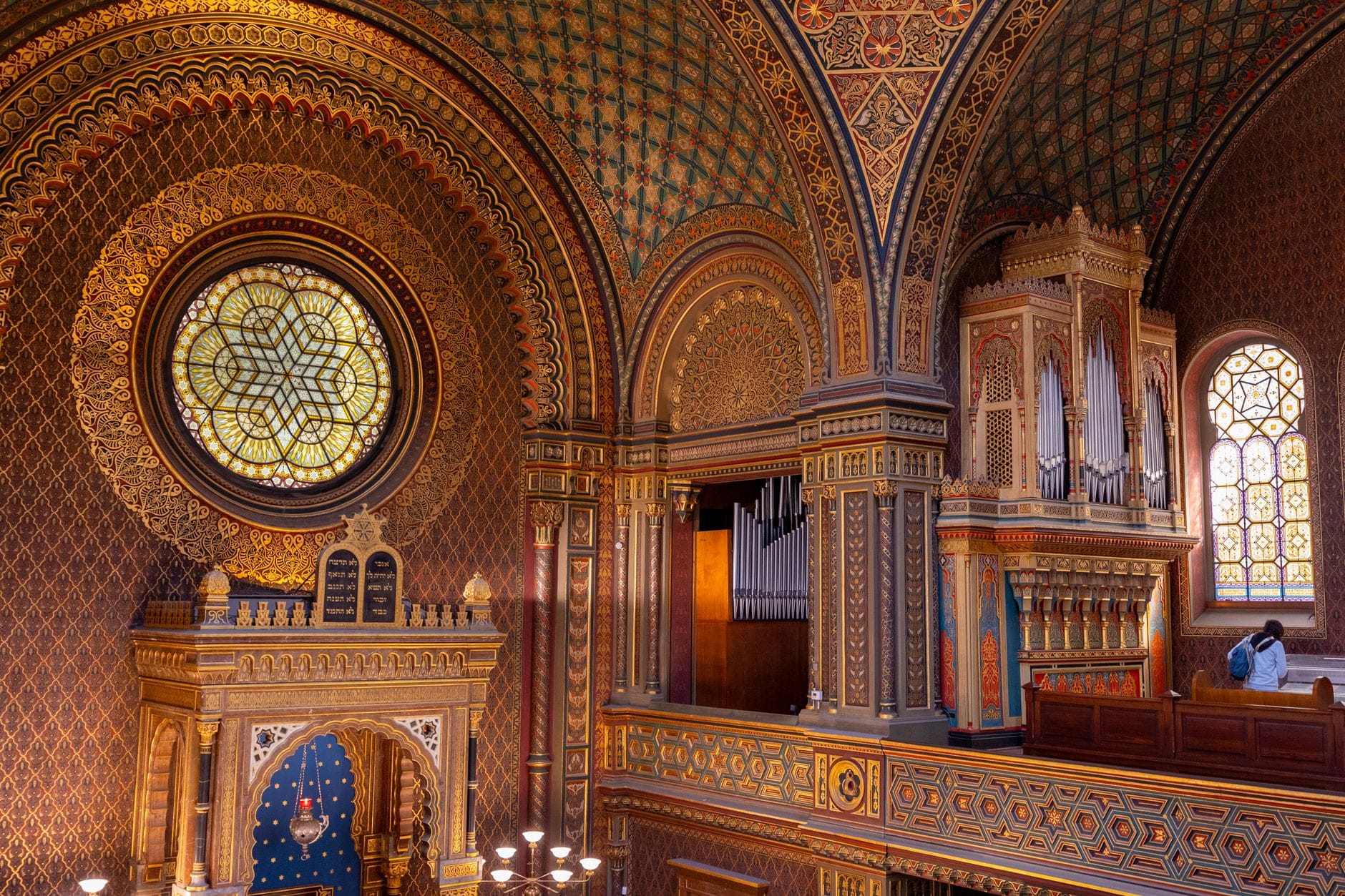 Bogate mauretańskie wnętrze Synagogi Hiszpańskiej w Pradze z ozdobnymi łukami, złotymi detalami, witrażowym oknem, organami i misternymi wzorami.