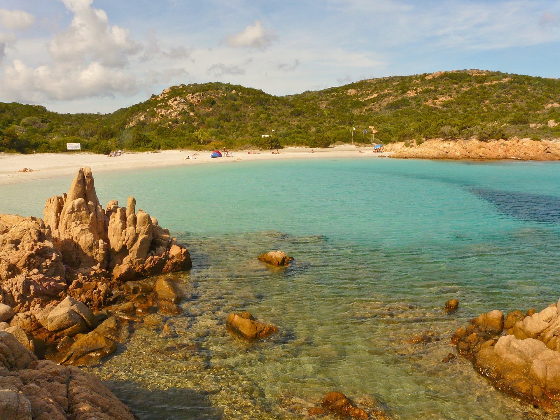 Klares türkisfarbenes Wasser, weißer Sandstrand und einzigartige Granitfelsen an der Spiaggia del Principe mit grünen Hügeln im Hintergrund.