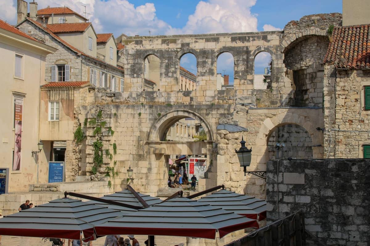 Alte Steinmauern und Bögen des Diokletianspalasts mit Menschen, die darunter spazieren, in der Altstadt von Split, Kroatien.