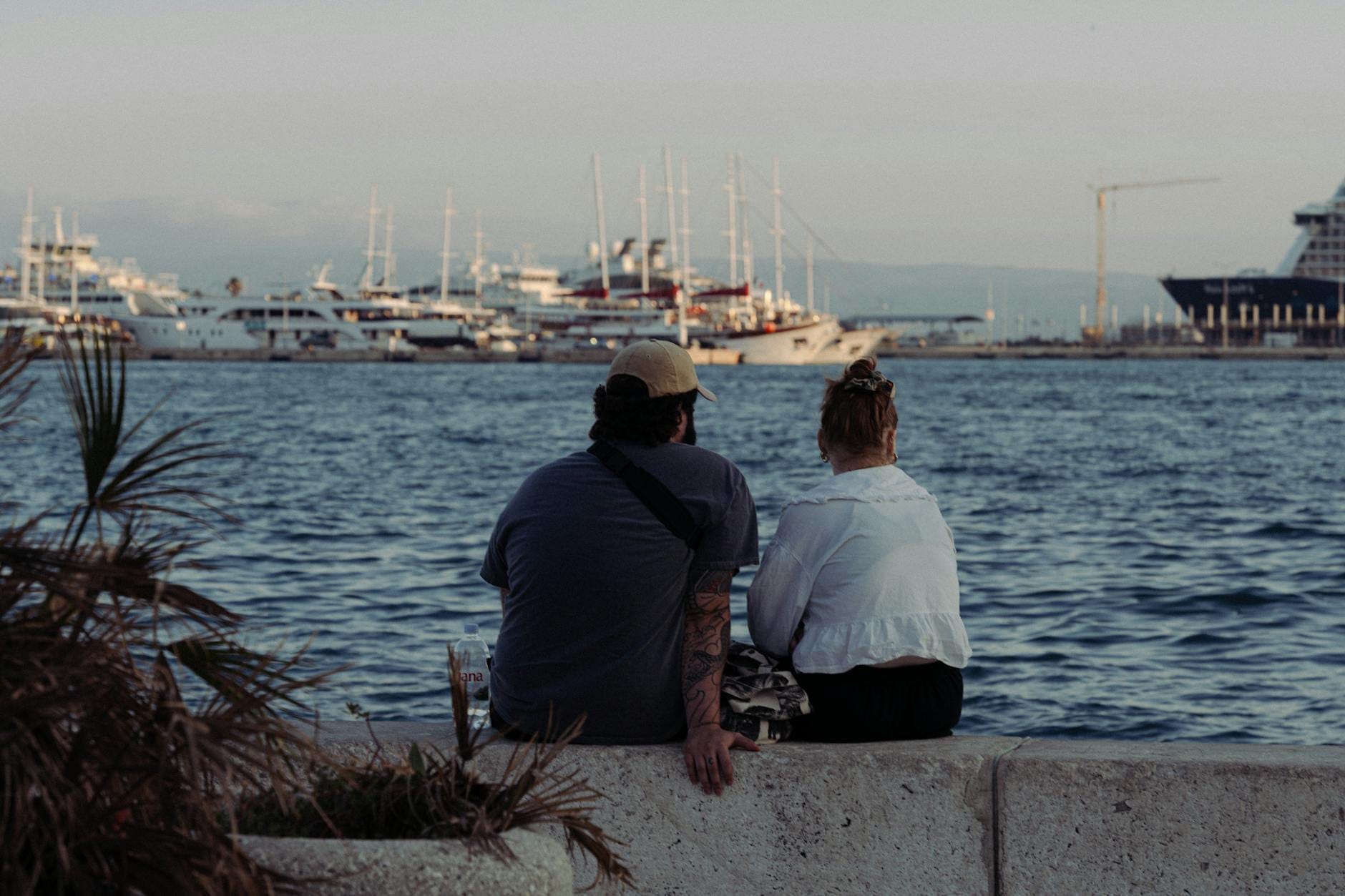 Um casal sentado junto ao calçadão de Split, contemplando o mar Adriático e os iates atracados ao pôr do sol.