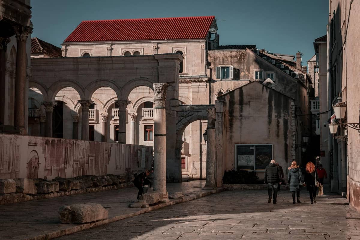 Menschen schlendern an alten Steinbögen und römischen Ruinen im historischen Zentrum von Split, Kroatien, vorbei, im dramatischen Nachmittagslicht.