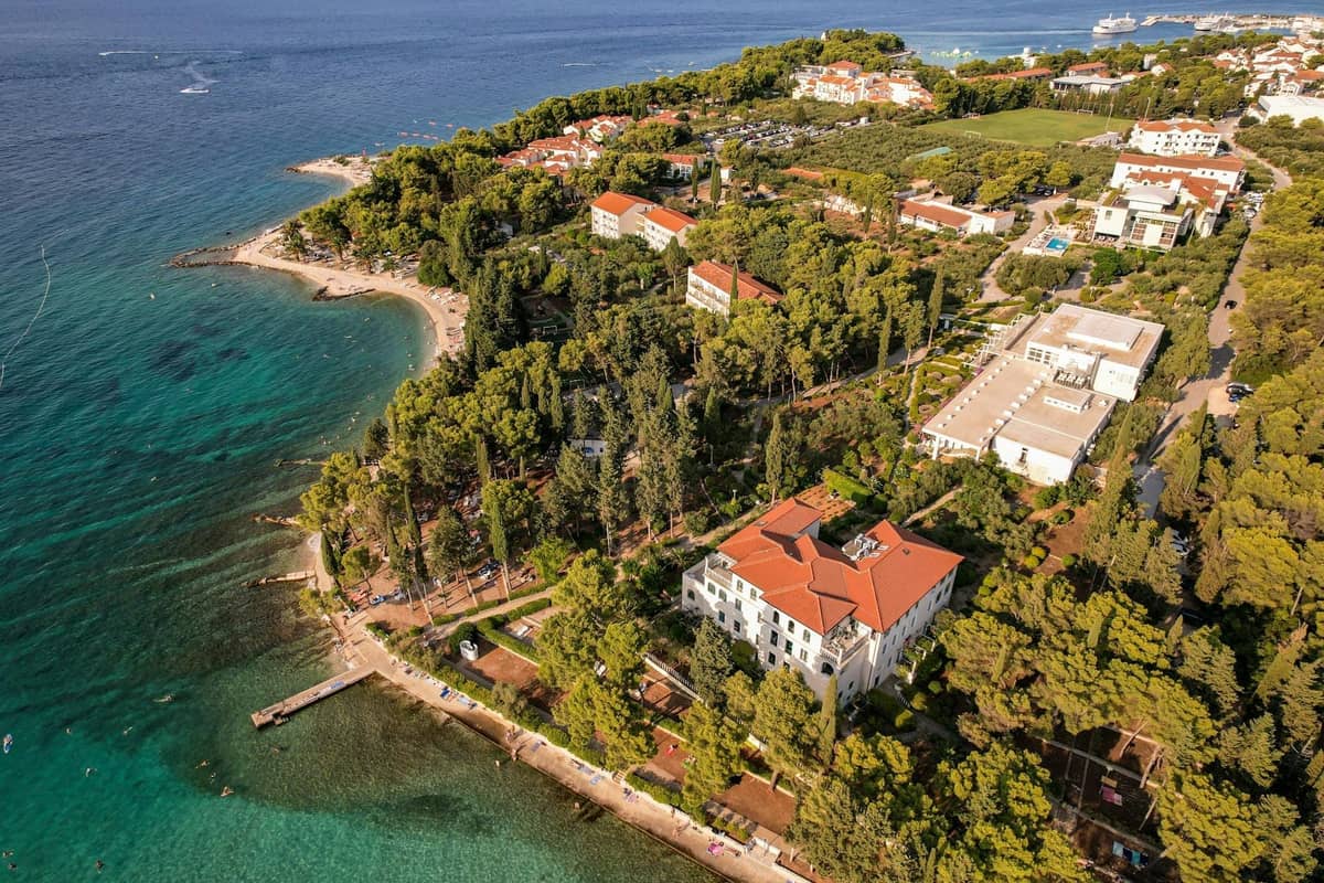 Luftaufnahme der Küste von Split im Sommer mit grünen Bäumen, Stränden, klarem blauem Meer und sonnenbeschienenen Gebäuden nahe dem Ufer.