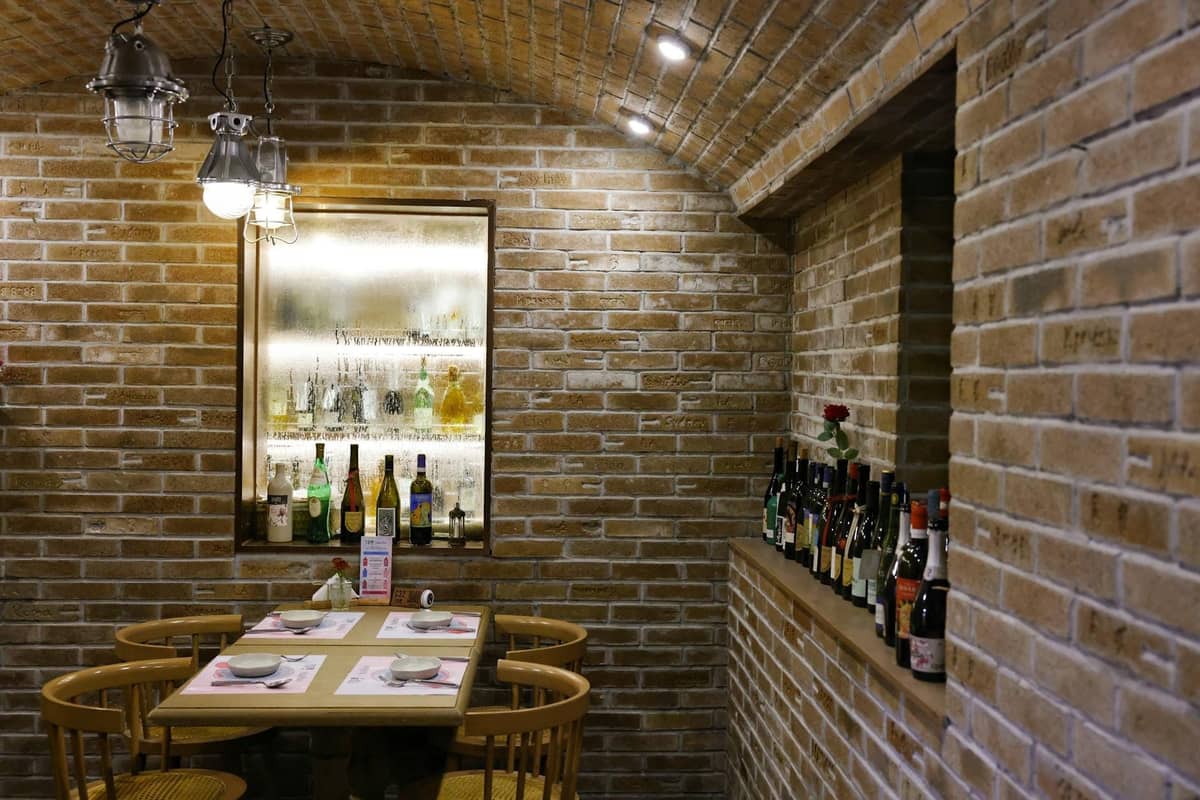 Gemütliche Bar mit Backsteinwänden, einem kleinen Tisch, Stühlen und verschiedenen Wein- und Spirituosenflaschen, die die Atmosphäre eines klassischen europäischen Altstadtkellers heraufbeschwören.