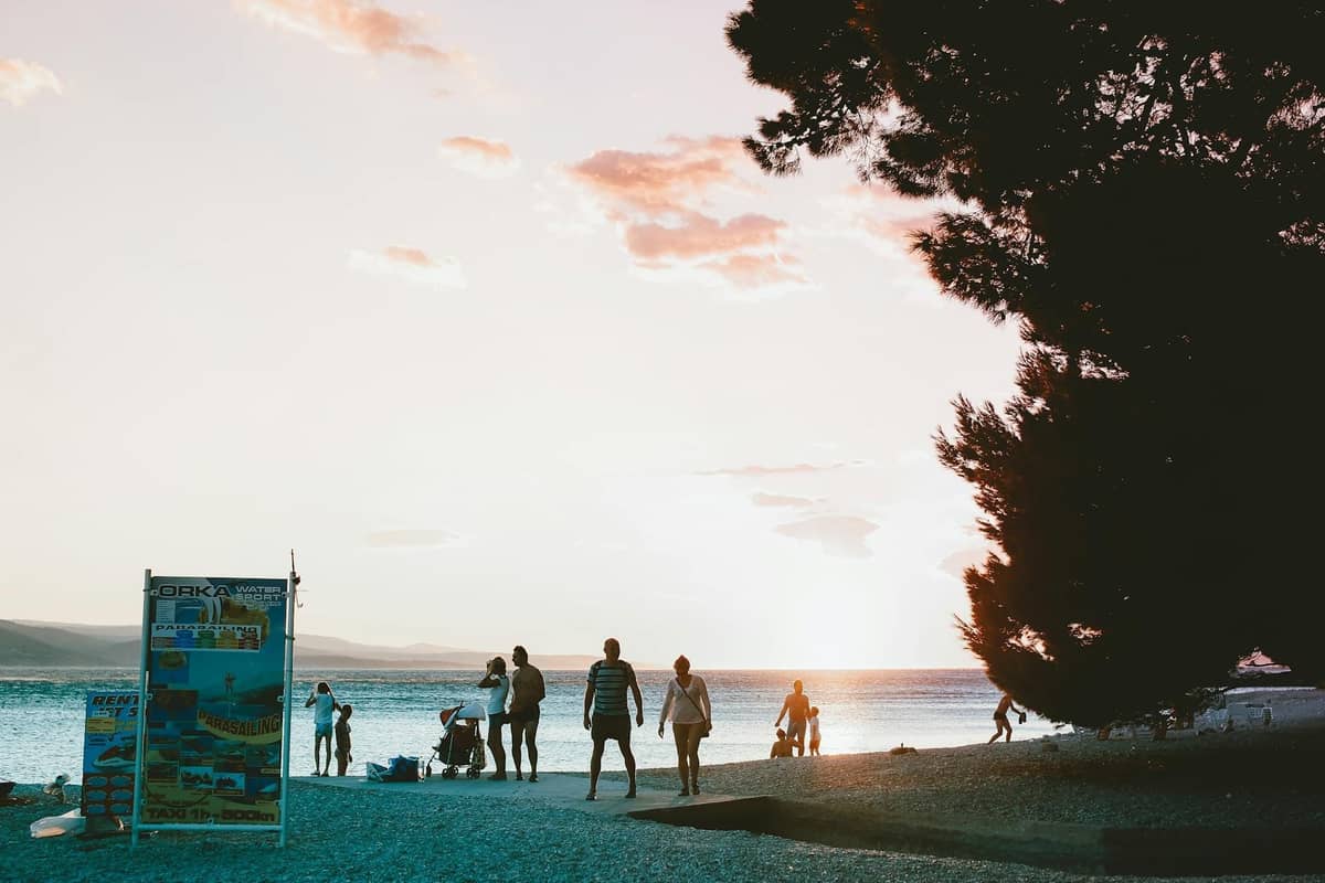 Menschen, die bei Sonnenuntergang entlang der Strandpromenade von Split spazieren und entspannen, mit einem lebhaften Himmel und ruhigen Adriawasser im Hintergrund.