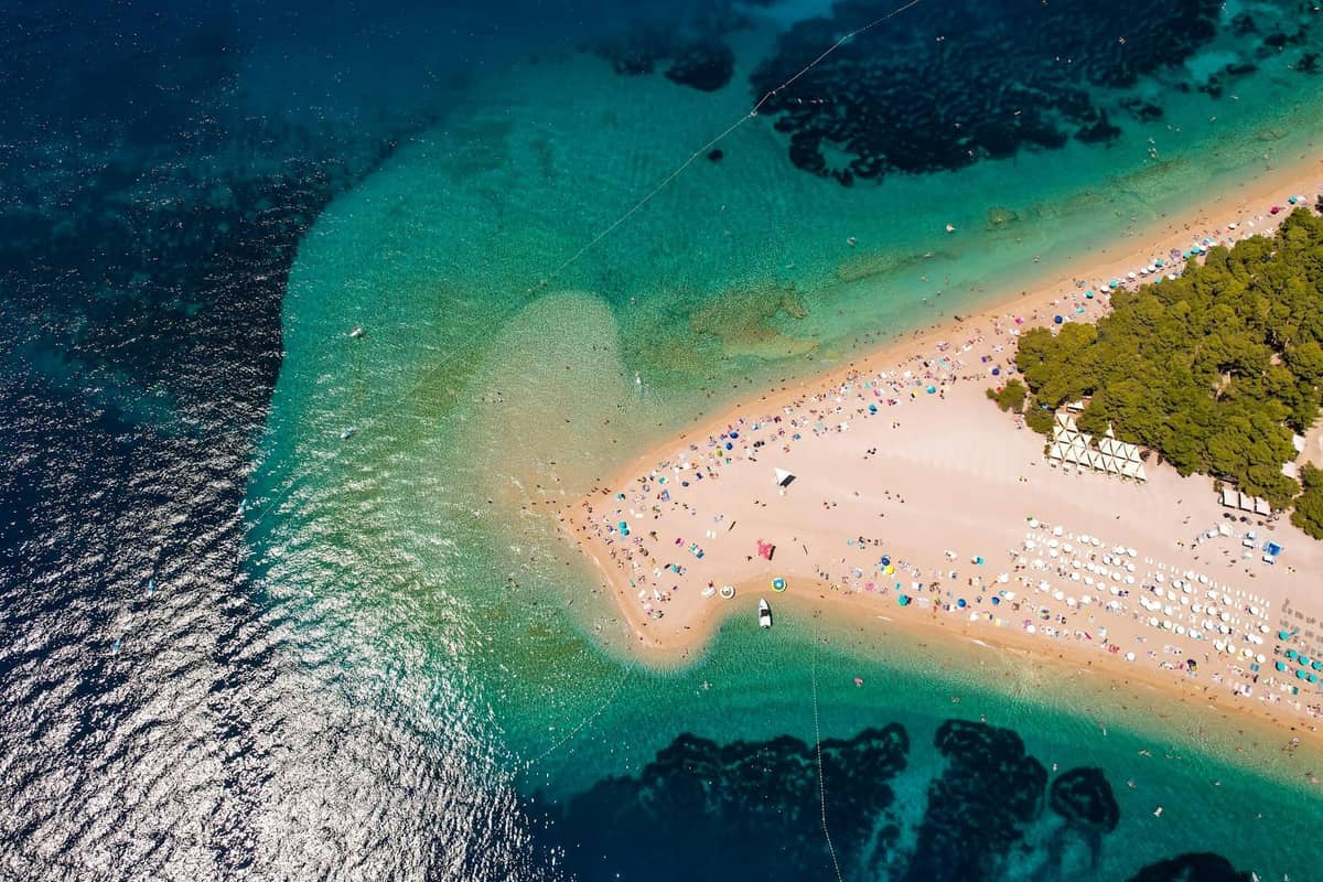 Luftaufnahme eines überfüllten kroatischen Strandes mit Sonnenschirmen, Sonnenanbetern und Schwimmern an einem sonnigen Sommertag.