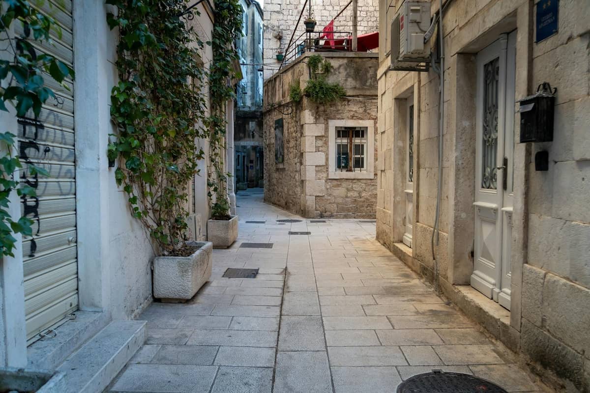 Enge, steingepflasterte Gasse, gesäumt von alten Steingebäuden und Grünpflanzen im historischen Zentrum von Split.