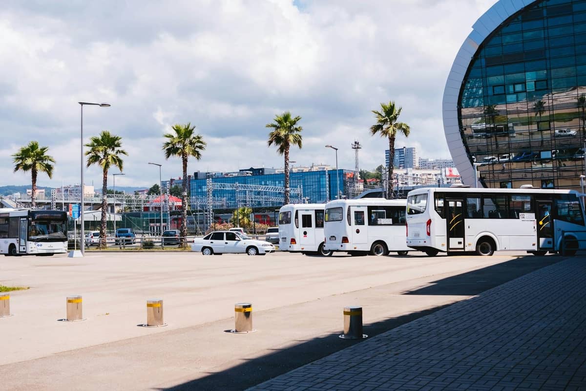 Modern bus station with white buses, palm trees, and contemporary glass building, likely in a Mediterranean city such as Split.